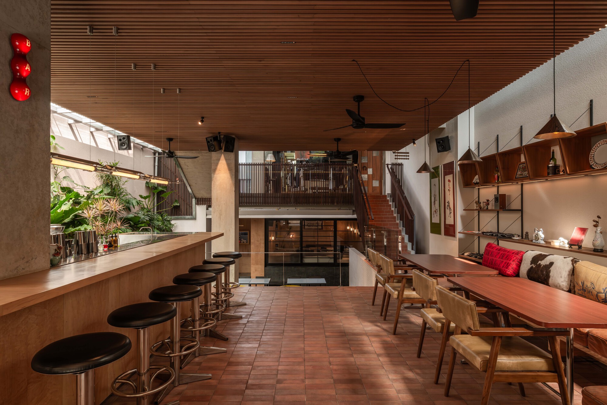 Open dining space with timber ceiling, long communal table, bar stools, and suspended pendant lights