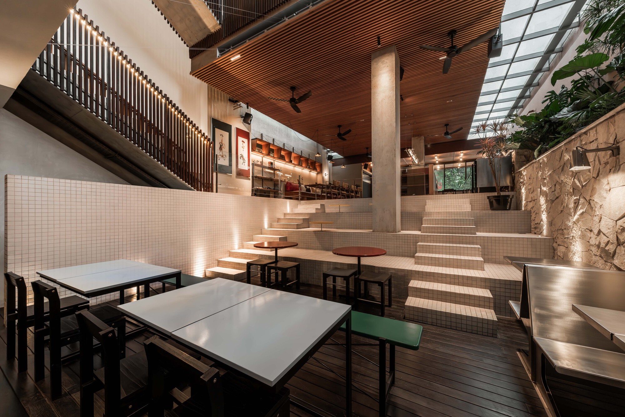 Interior dining area with stepped seating, white tile walls, and a timber slatted ceiling