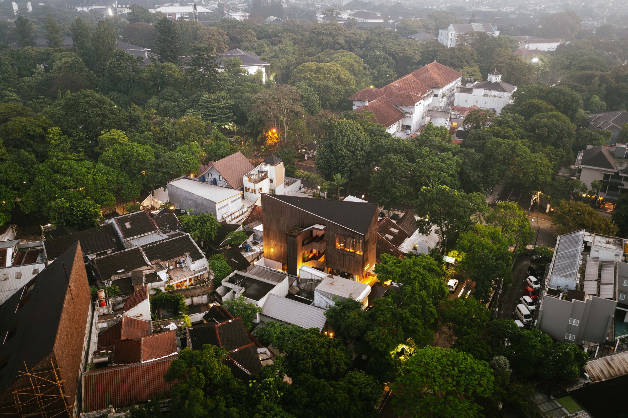 Aerial view of a timber and concrete tower rising among red-tiled roofs and dense trees at dusk