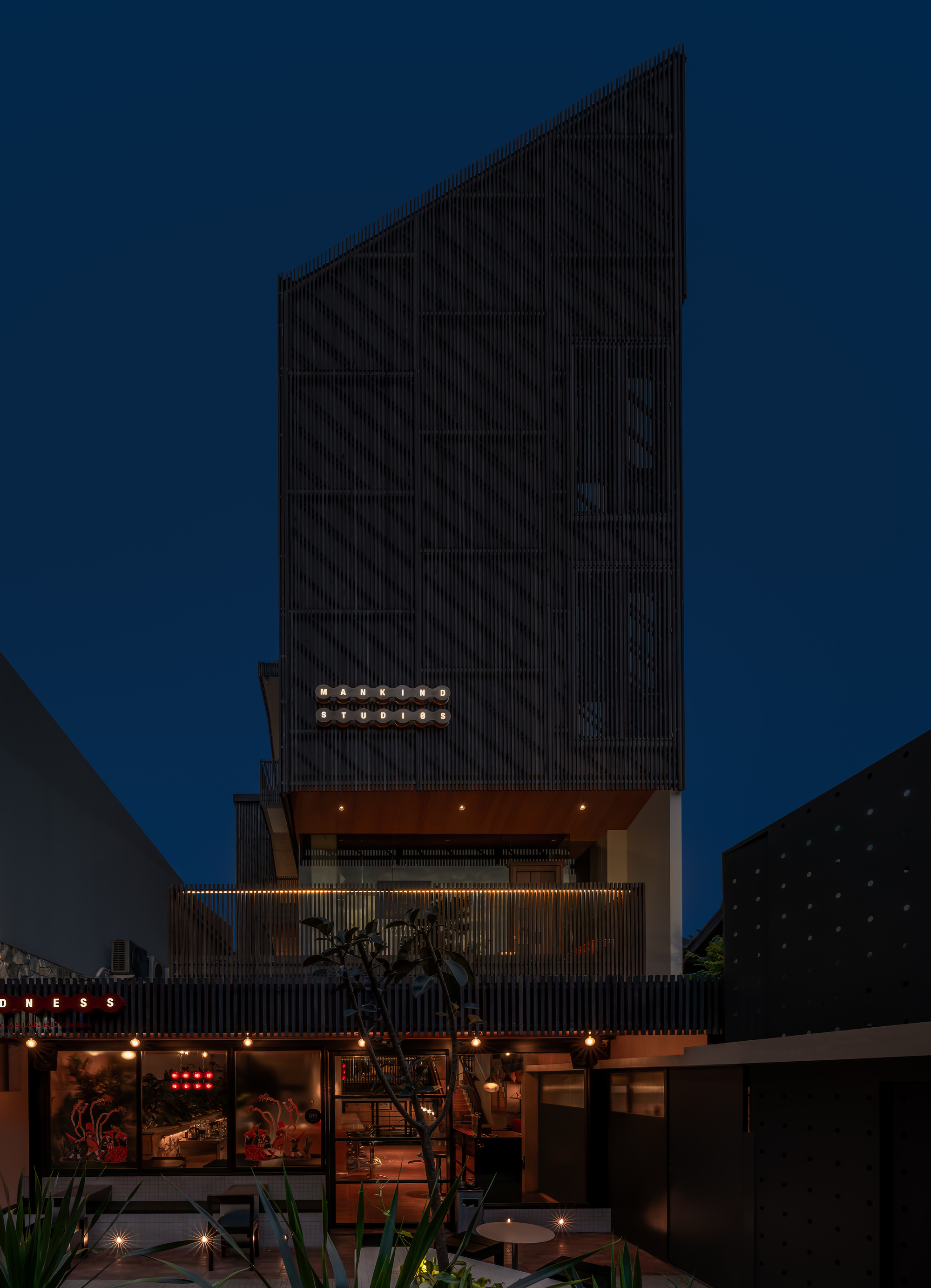 Night view of the facade with vertical slats, recessed balconies and string lights against a deep blue sky