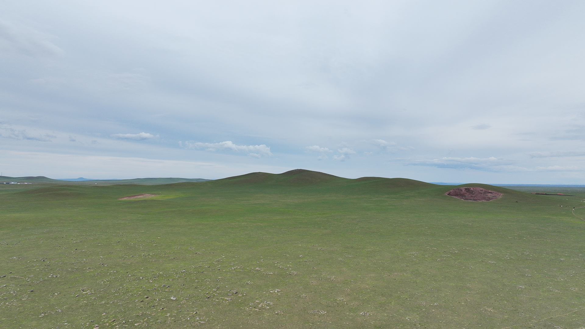 Original site photograph showing the C-shaped extinct volcano in the green grassland