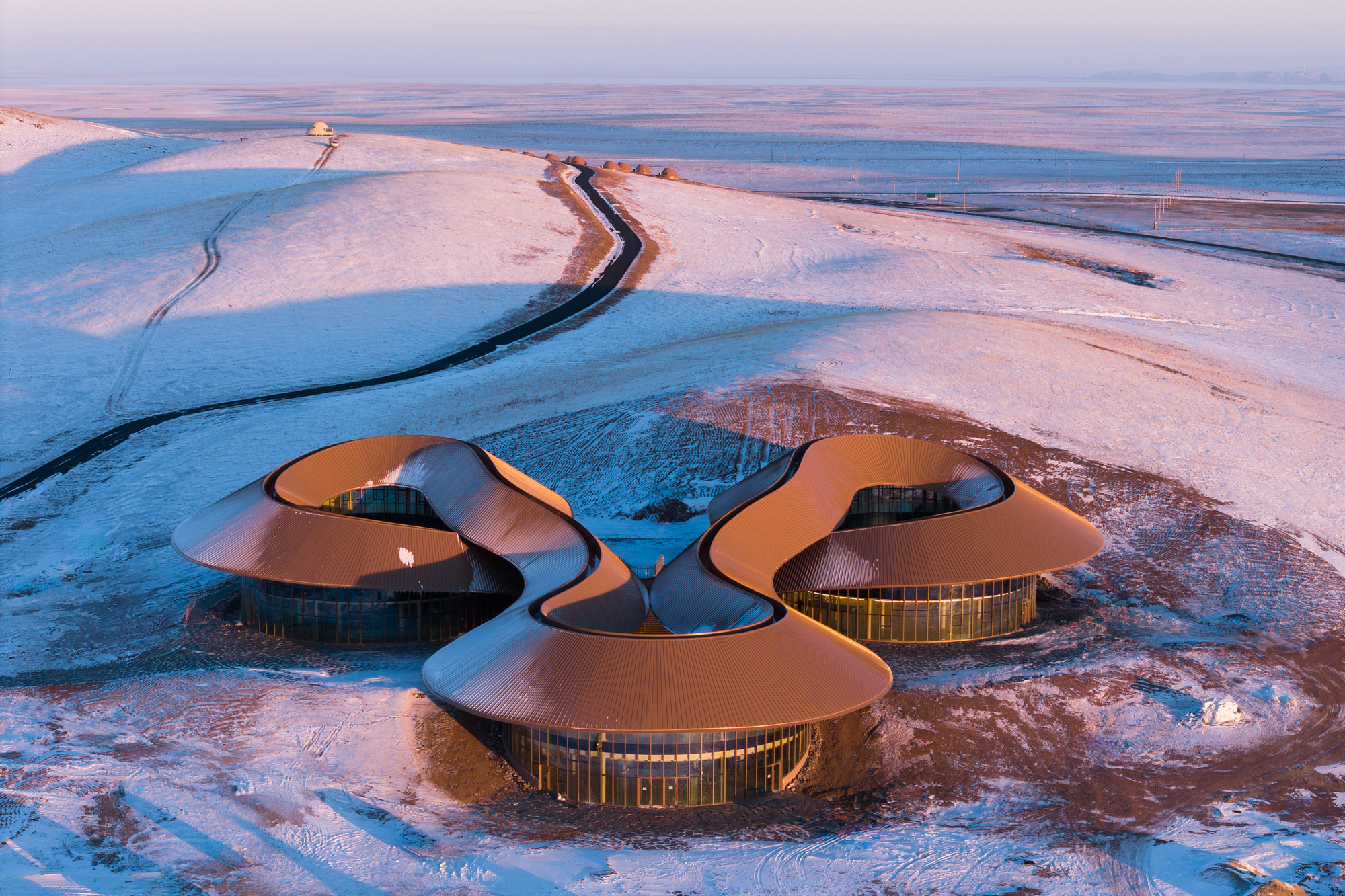 Sunset aerial of the warm-toned roof against the snow with a road approaching