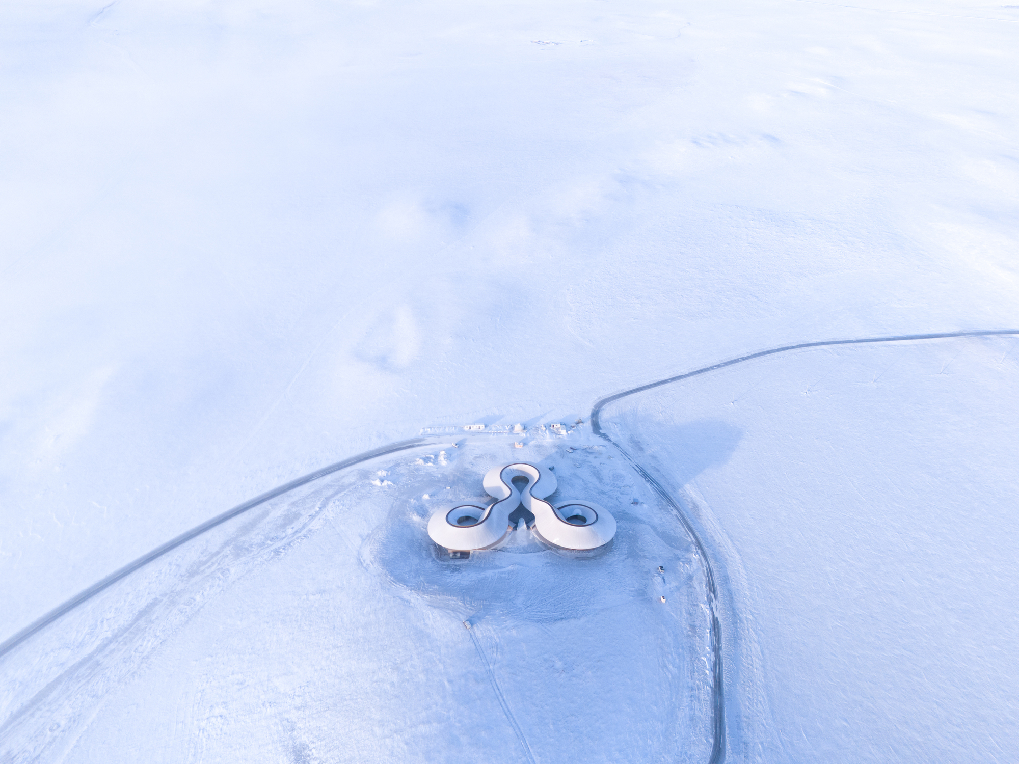 Top-down aerial showing the building as a tiny mark on the vast snowfield