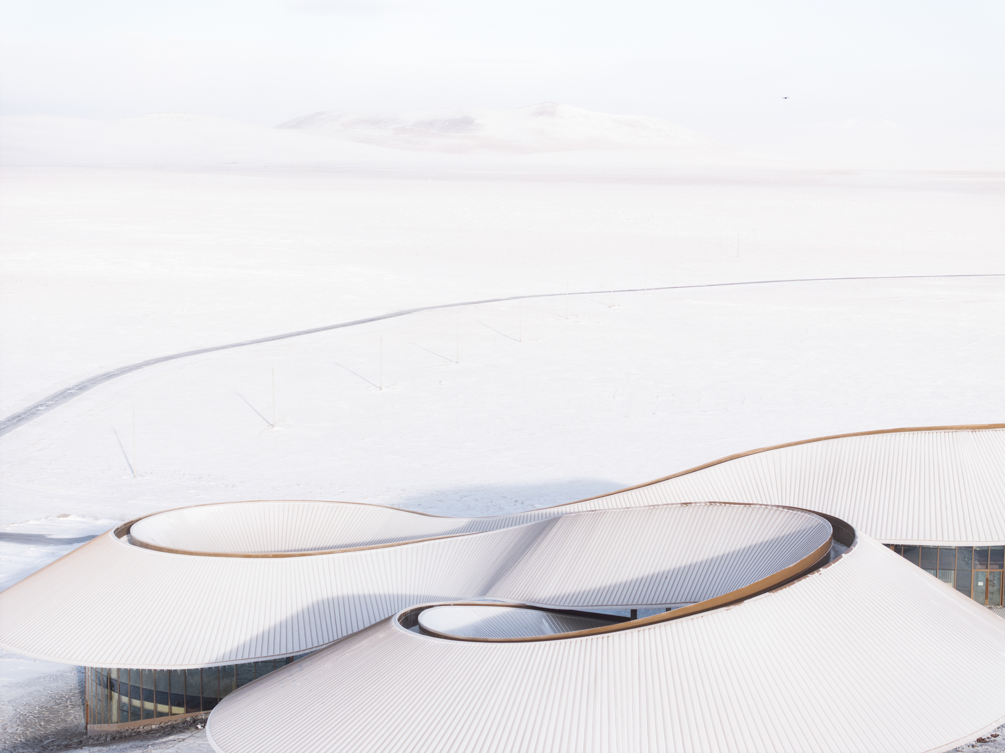 Aerial of two lobes of the roof meeting around a central skylight in heavy snow