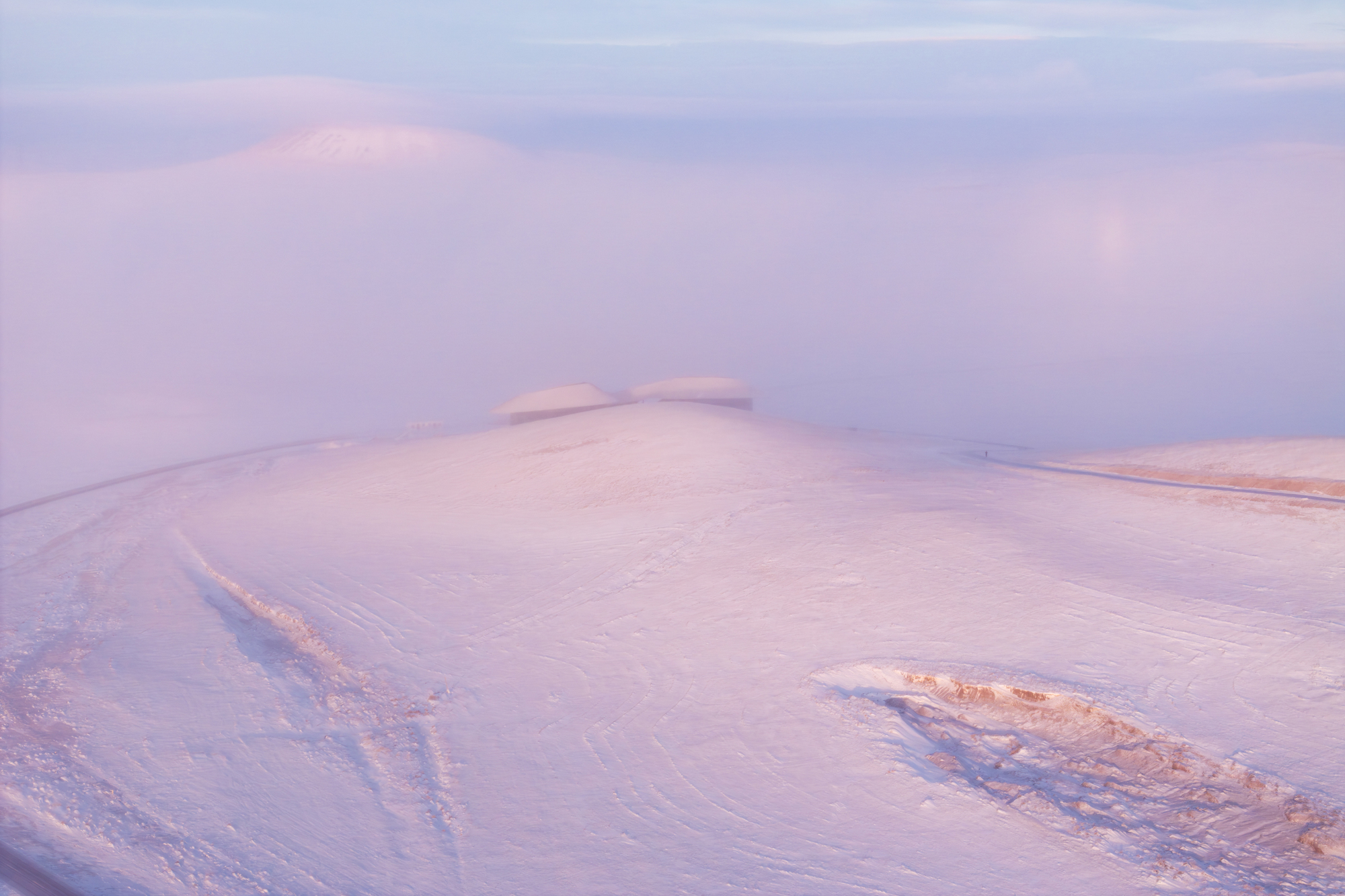 Distant view of the building tucked into a snowy ridge under pink sunset clouds