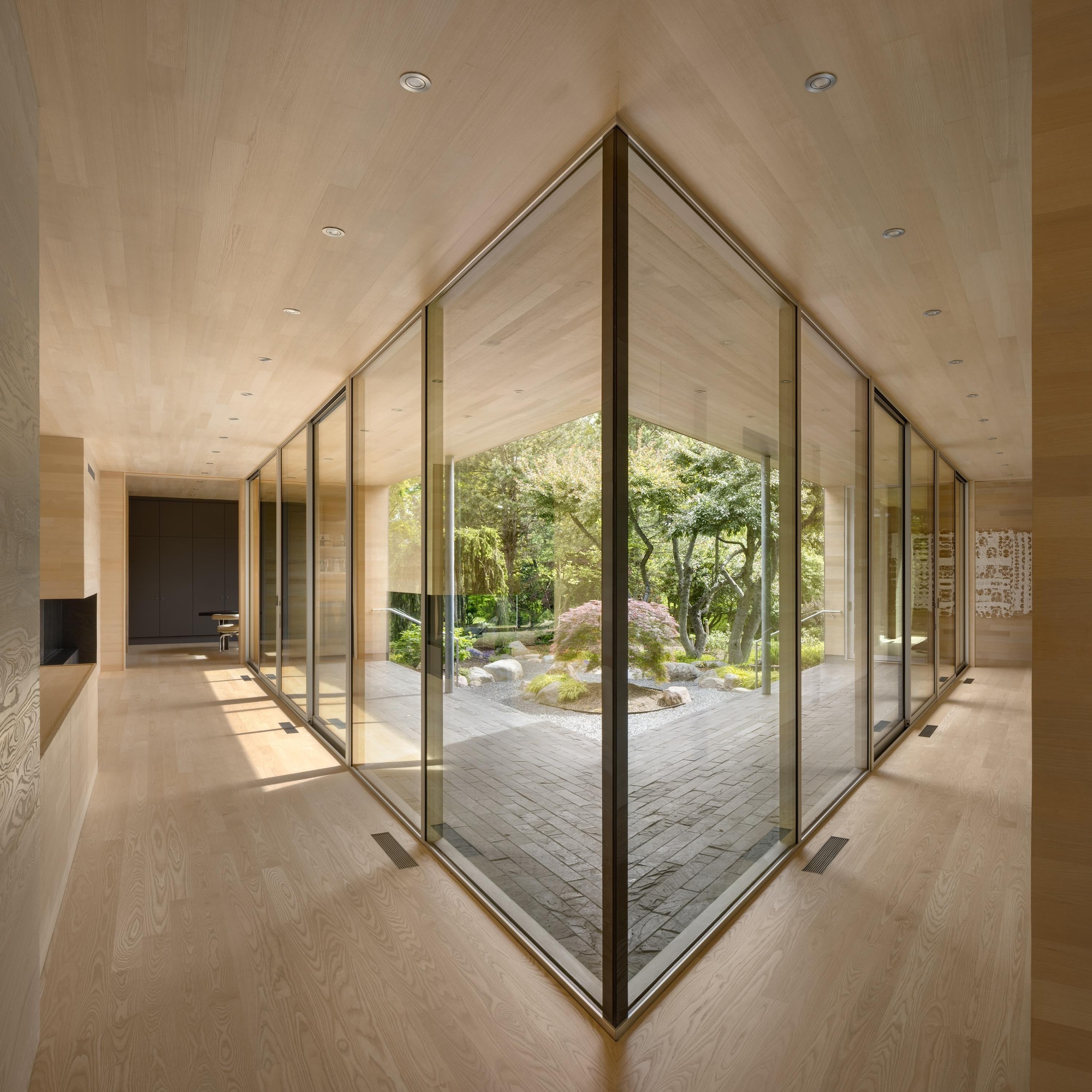 Corner glass walls framing an interior courtyard with brick paving and moss under dappled light