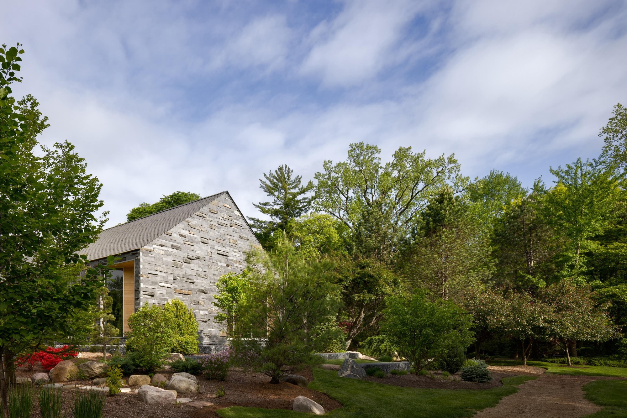 Reclaimed white brick gable end rising from a landscaped garden beneath a cloudy spring sky