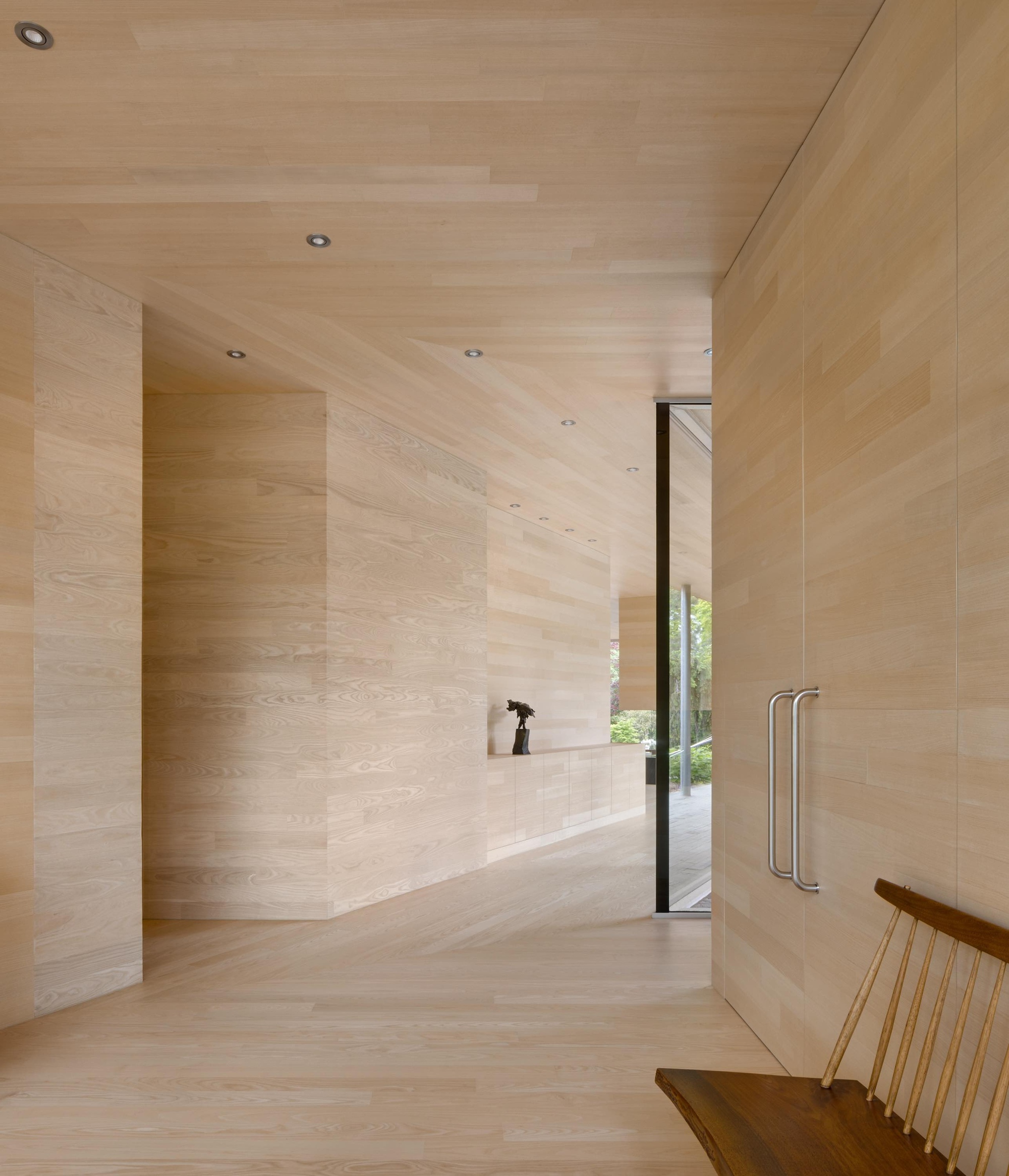 Light-toned wood-clad entry hallway with recessed lighting and glazed door to exterior garden