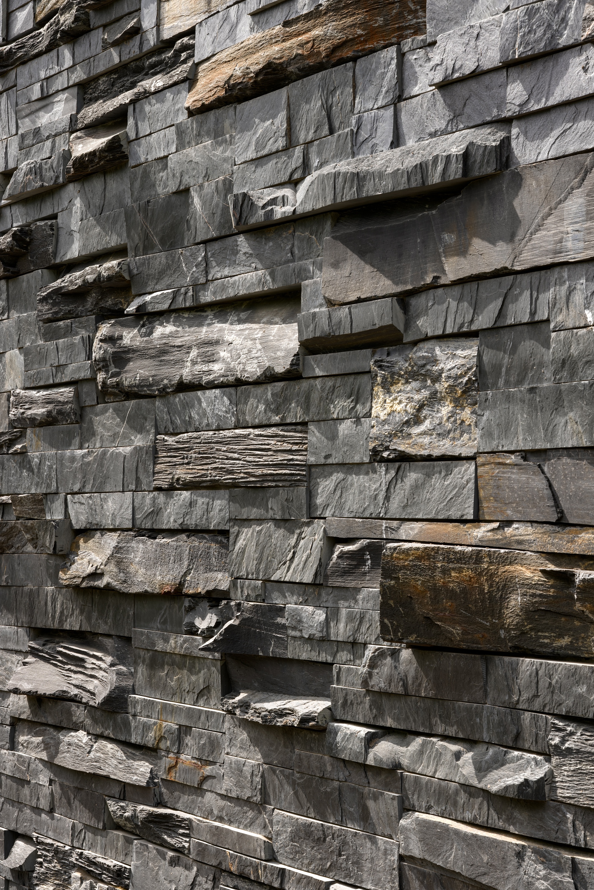 Close-up of stacked slate cladding with rough-hewn edges and varied grey and brown tones in natural light