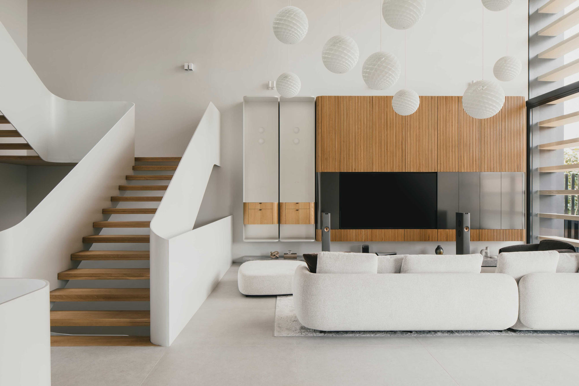Double-height living room with cantilevered timber staircase and ribbed wood media wall beneath spherical pendant lights