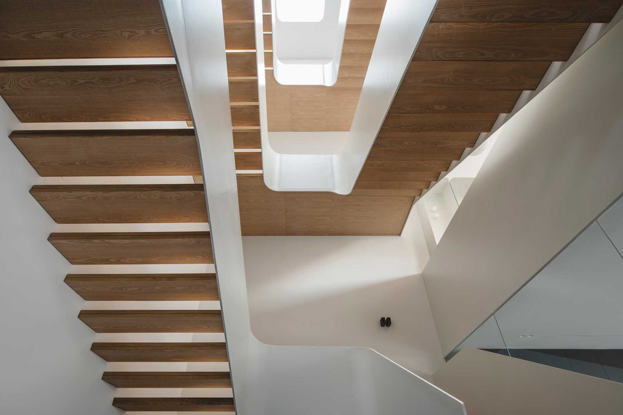 Upward view of timber staircase with glass balustrade beneath a coffered wooden ceiling with skylights