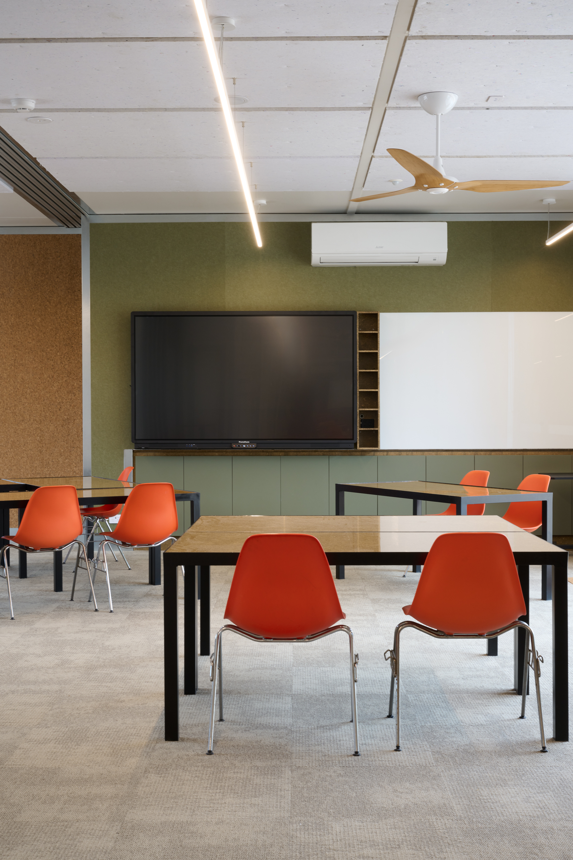 Classroom interior with orange chairs, a large screen on a green wall and cork pinup panels