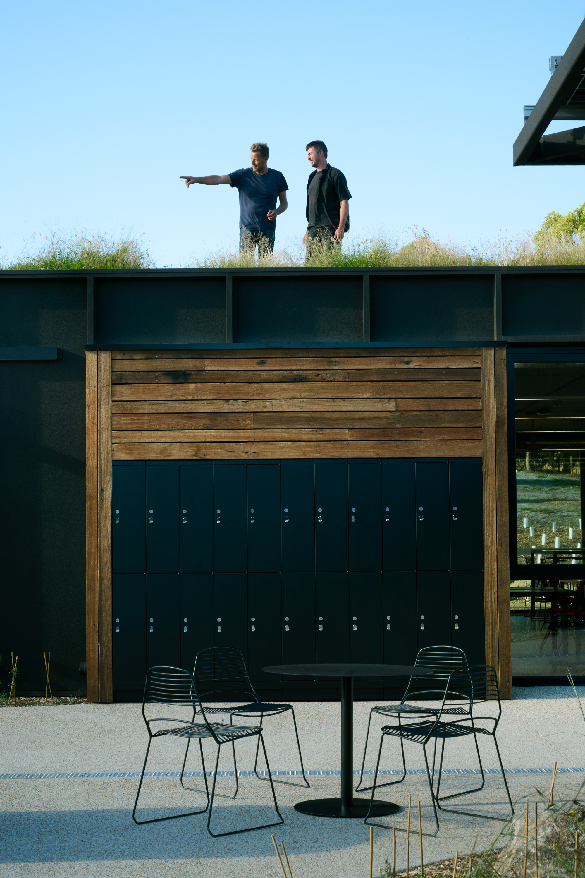 Two people on the green roof above the timber locker wall with students seated on the courtyard below