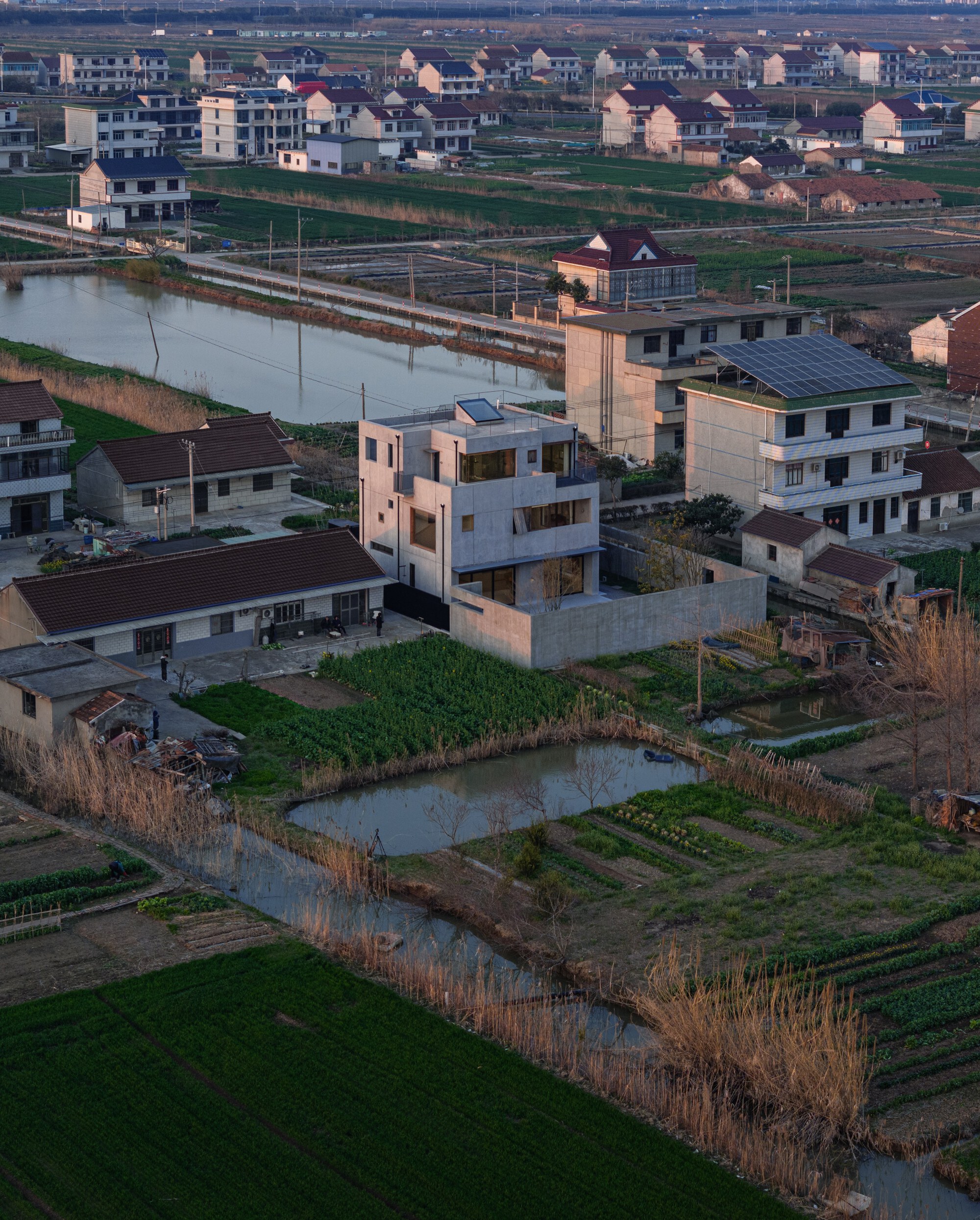 Aerial view of the concrete residence amid agricultural plots and water channels at dusk