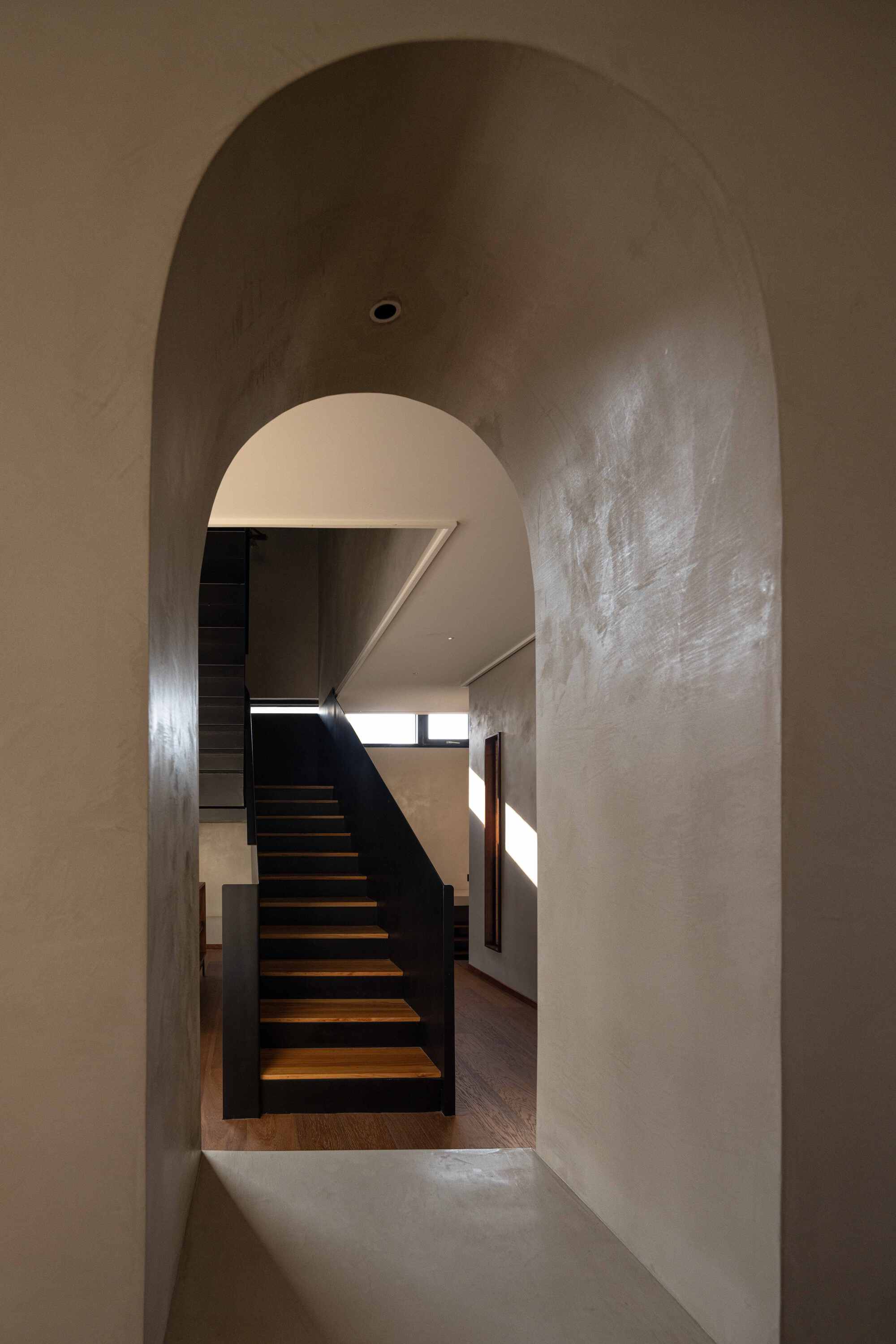 Arched passageway framing the black steel staircase with timber treads and afternoon light from above
