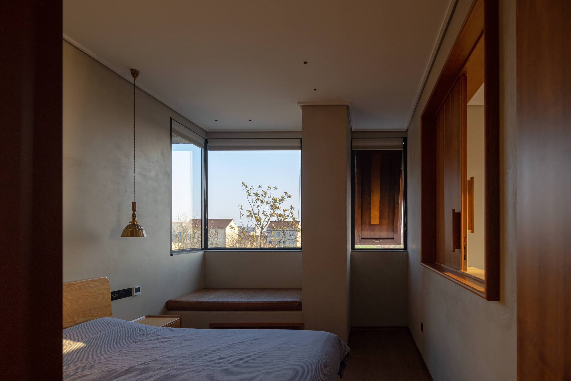 Bedroom with corner windows, timber built-in desk and pendant light in afternoon sun