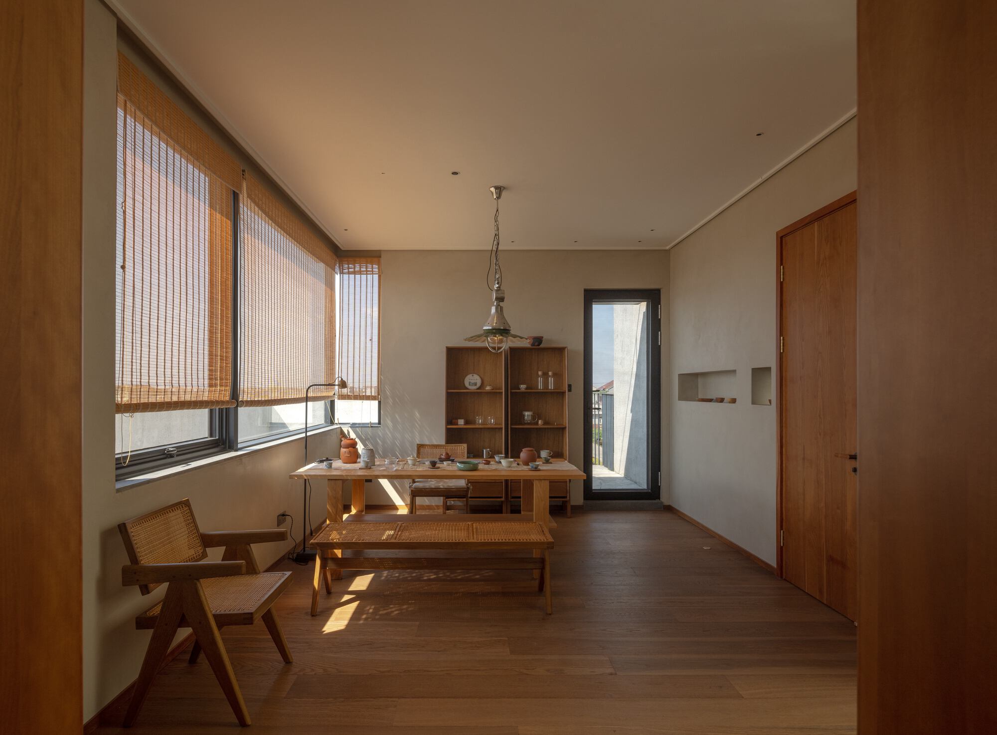 Dining room with timber table and bench, bamboo roller shades filtering afternoon sunlight through corner windows