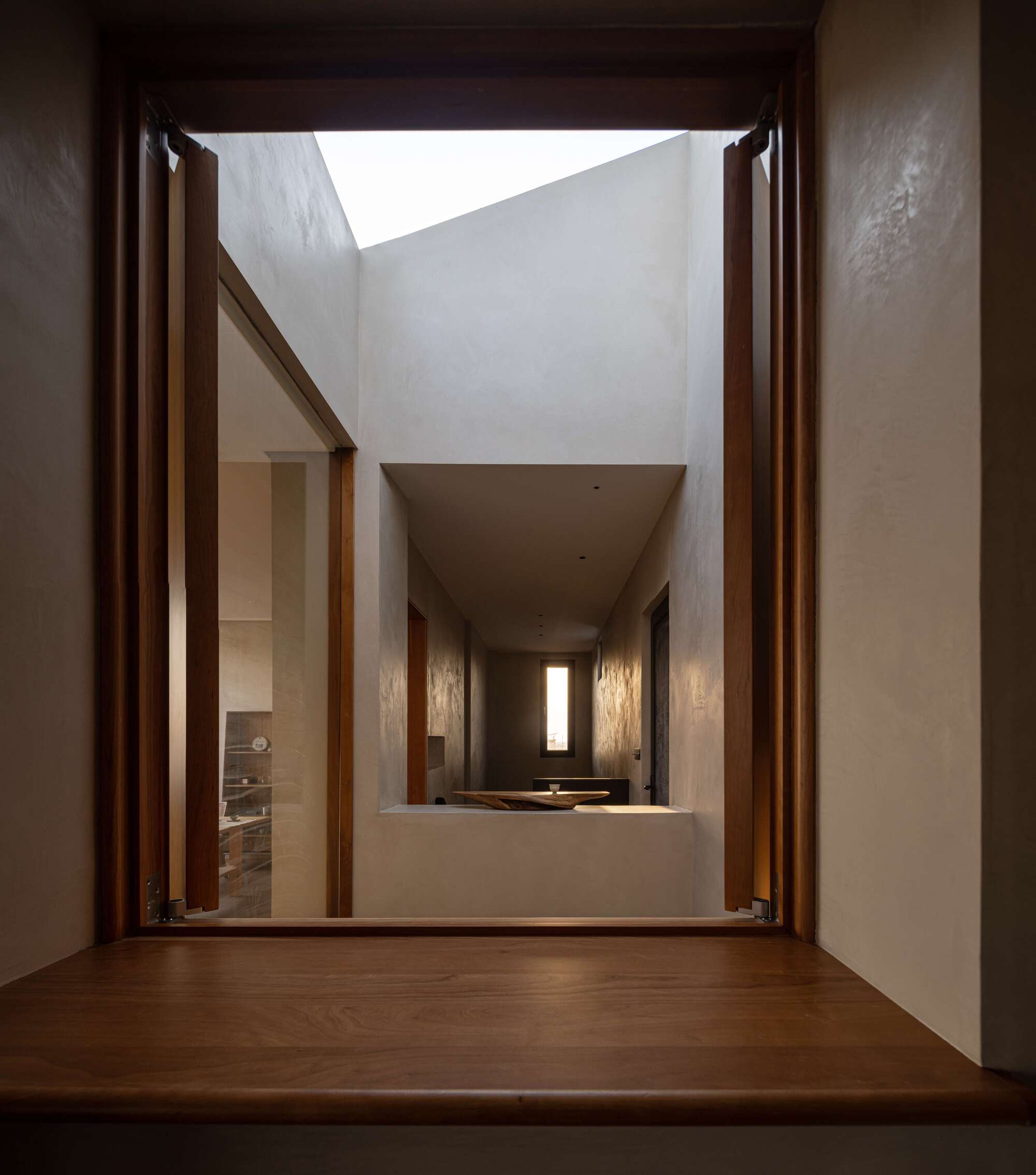 Timber-framed doorway opening to a double-height courtyard with white plastered walls and clerestory skylight