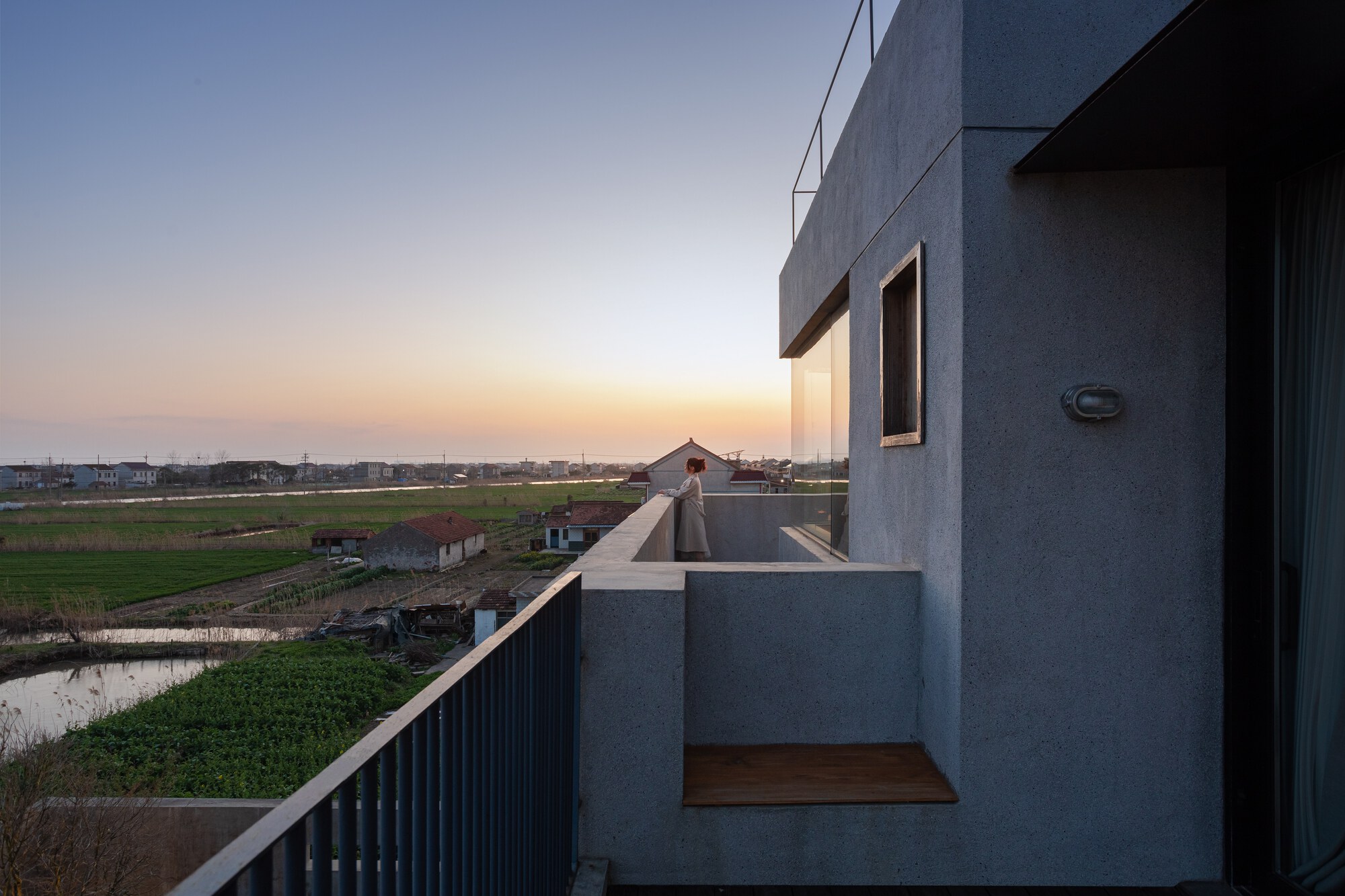 Rooftop terrace with recessed timber seating nook overlooking agricultural fields at sunset