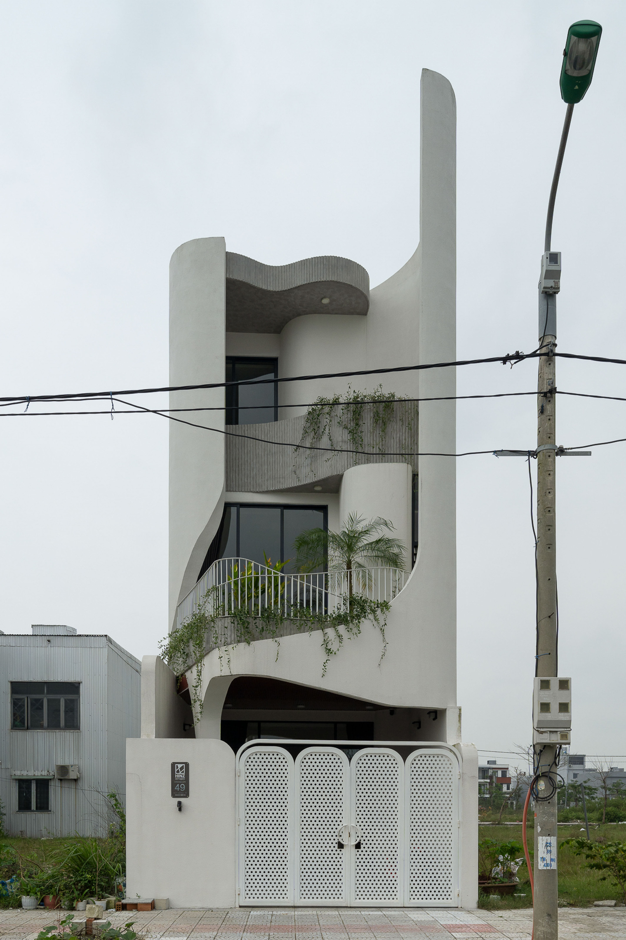 Street view of the white sculptural facade with curved balconies, planted terraces and perforated gate panels