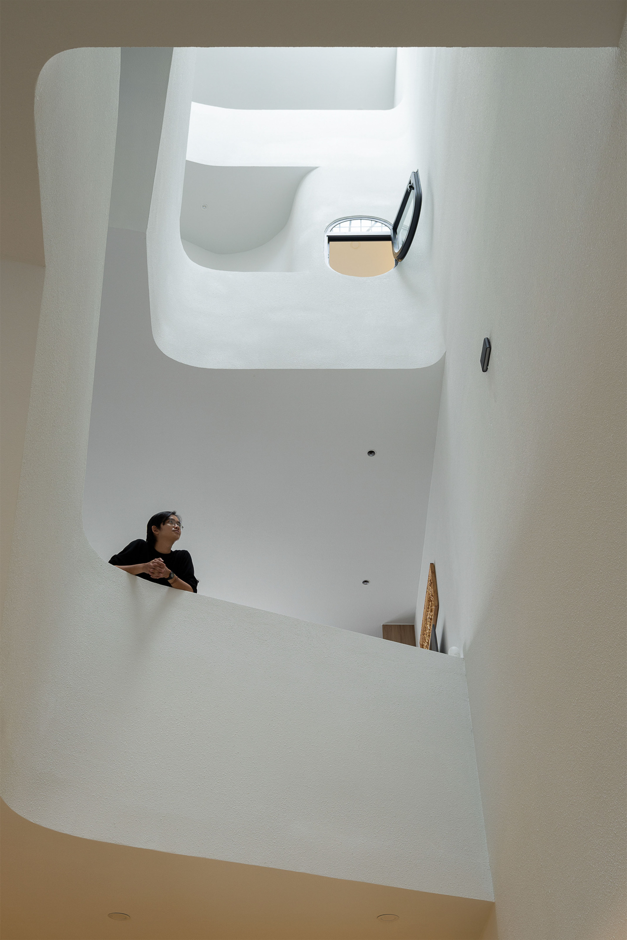 Vertical view of white stairwell with curved openings and person leaning over upper landing