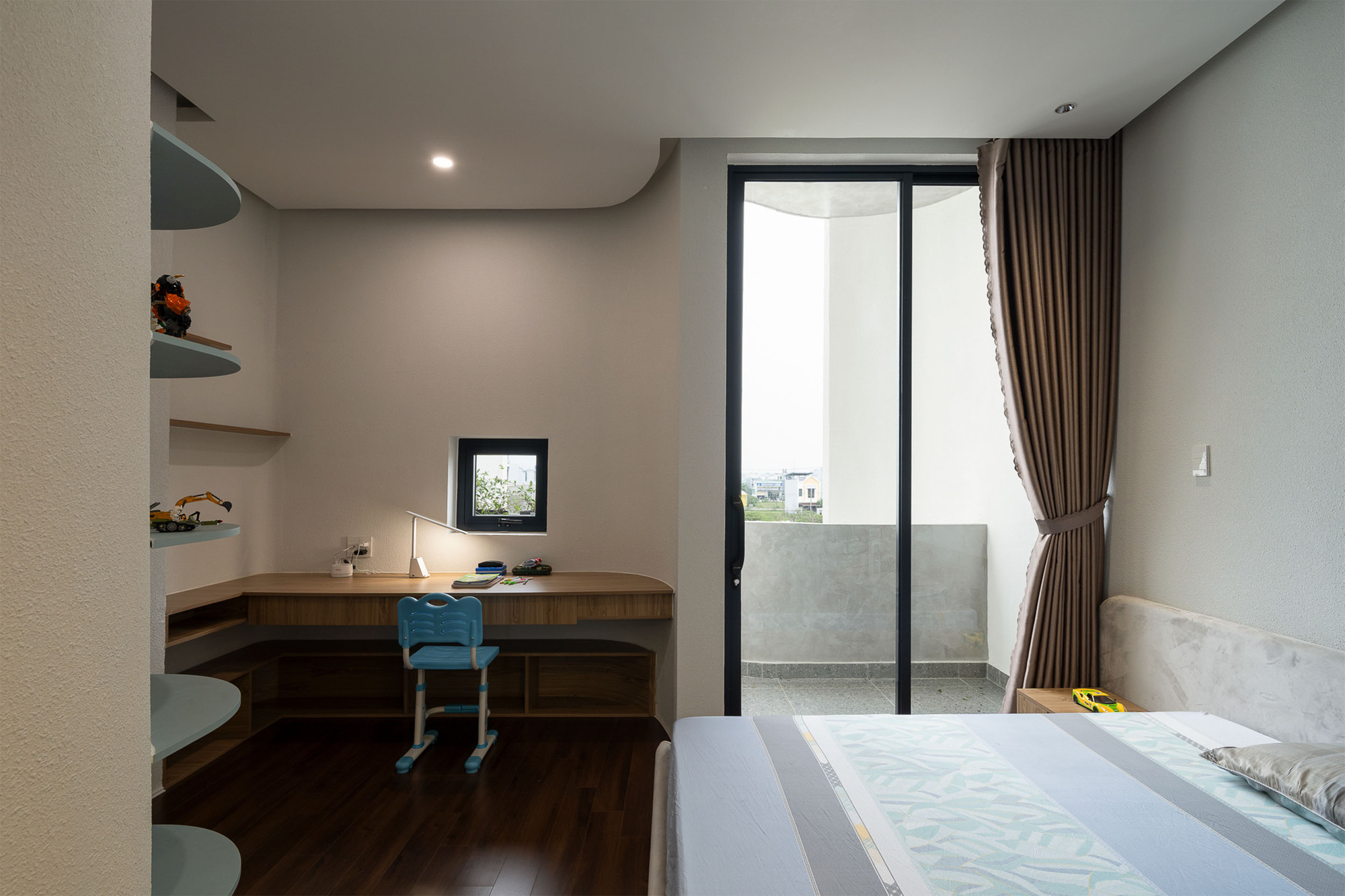 Study nook with timber desk and blue chair beside glazed door opening to balcony