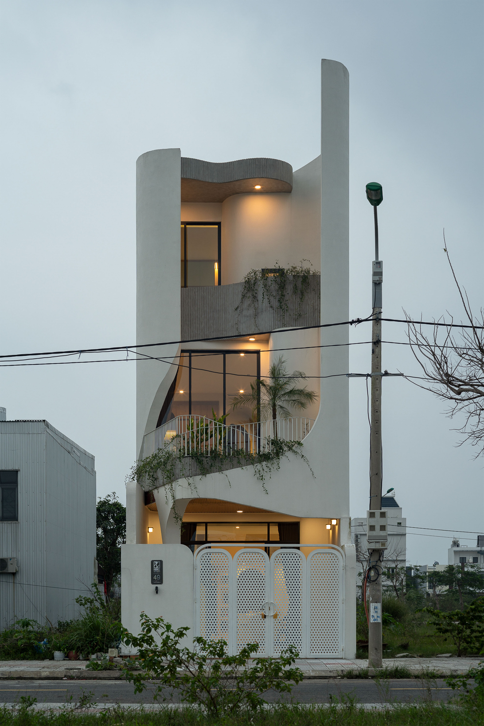 Three-storey white facade with curved parapet and planted balconies at dusk under power lines