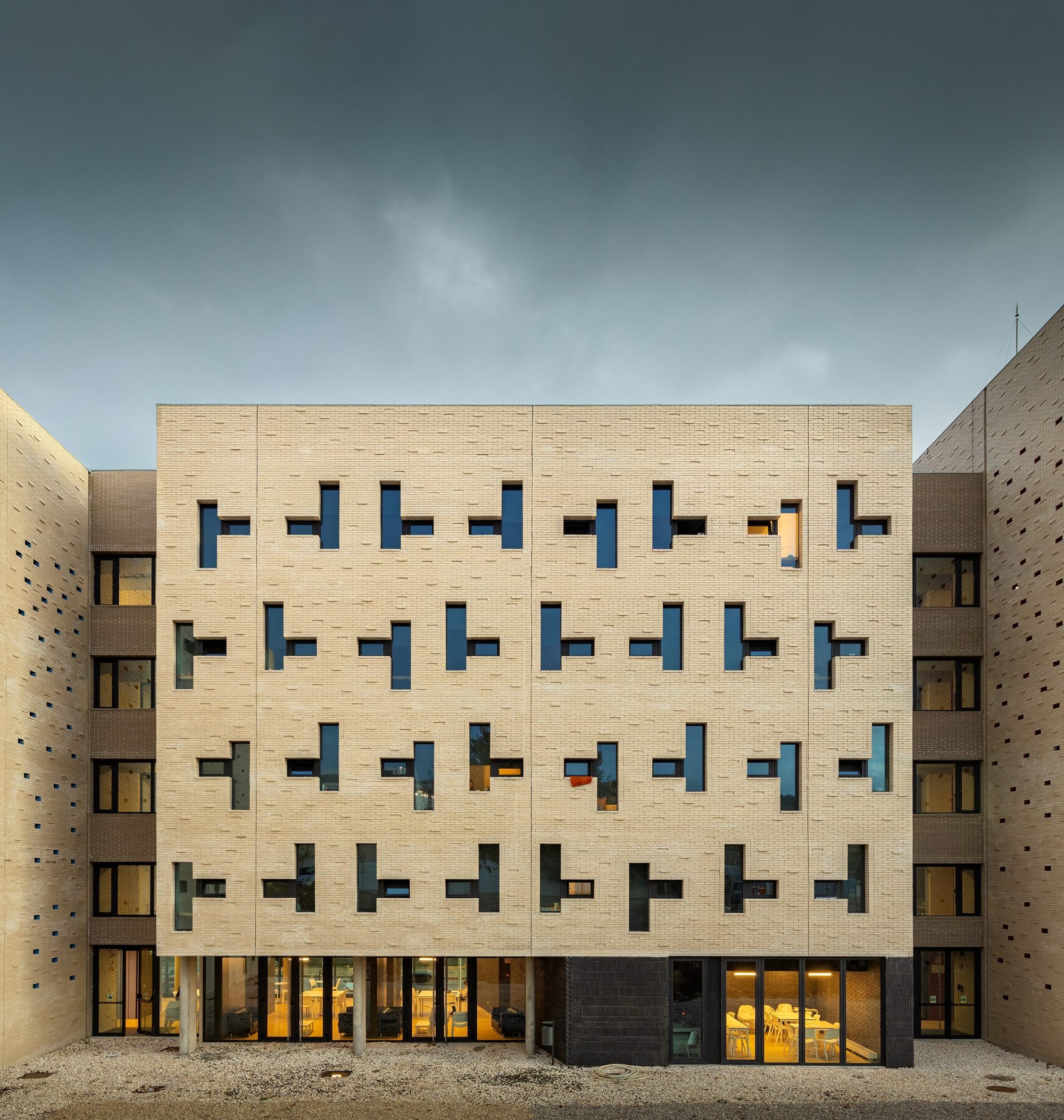 Courtyard facade with buff brick and irregular window openings under overcast skies