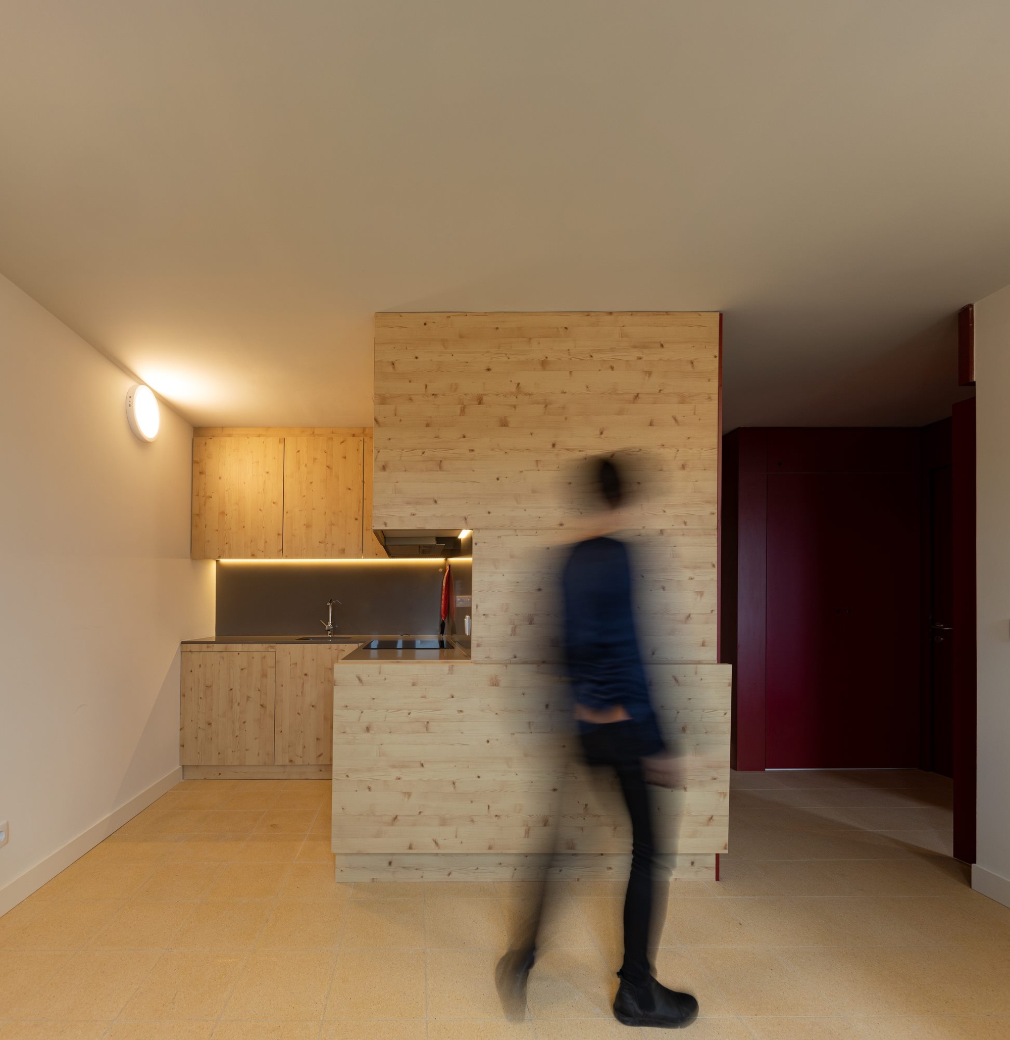 Compact kitchenette with timber cabinetry and a blurred figure in motion