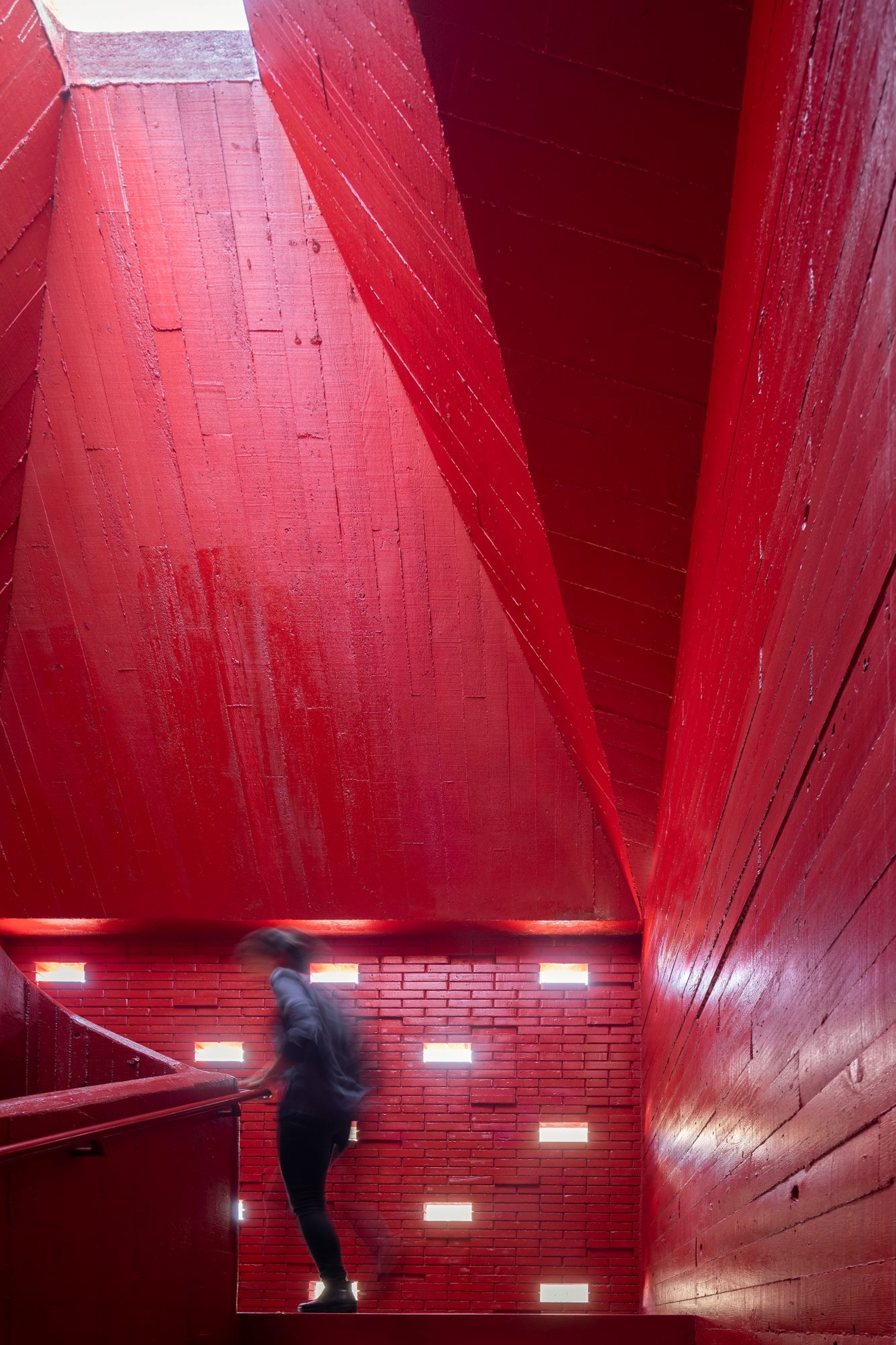 Stairwell clad entirely in red-painted timber with a descending figure