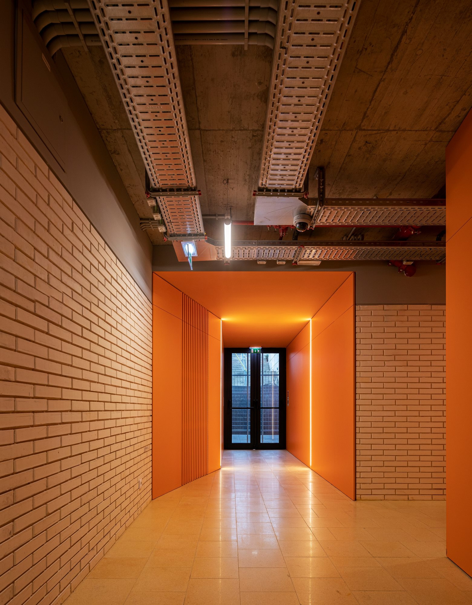 Orange painted corridor framed by cream brick walls with exposed concrete ceiling and terracotta panels
