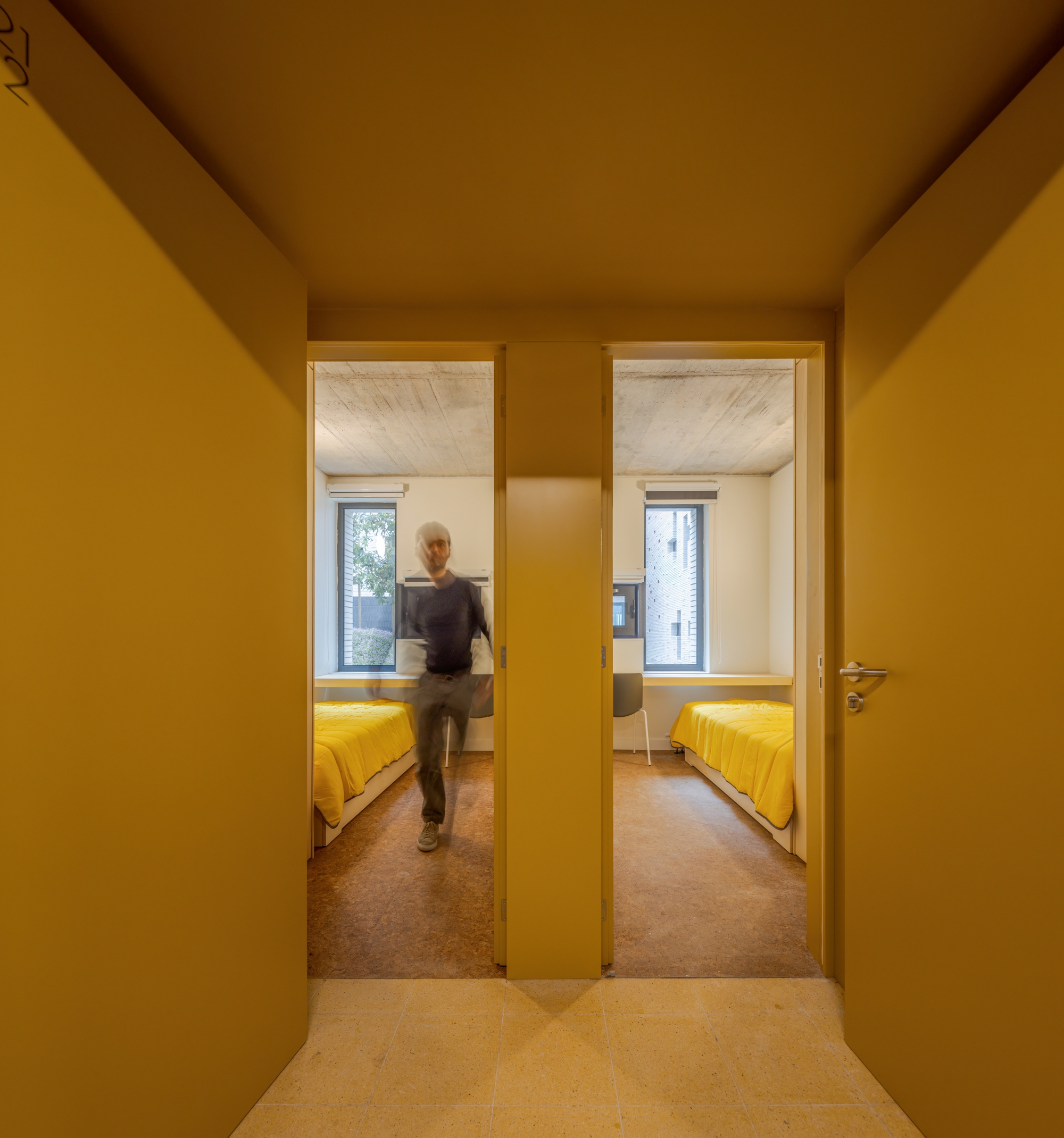 Mustard hallway looking through two doorways into bedrooms with yellow bedding and a person passing through