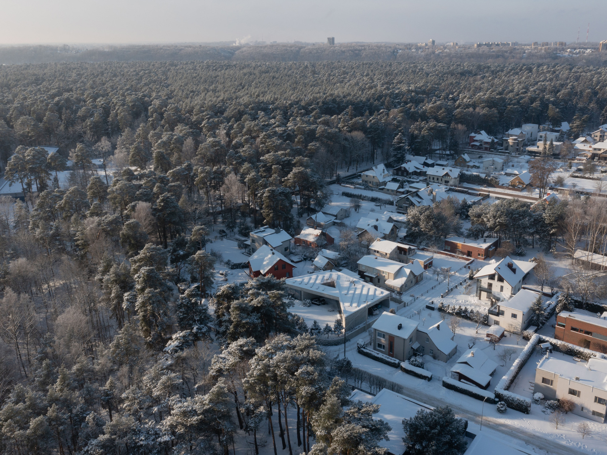 Drone view of the faceted roof among neighboring houses in a forested winter landscape