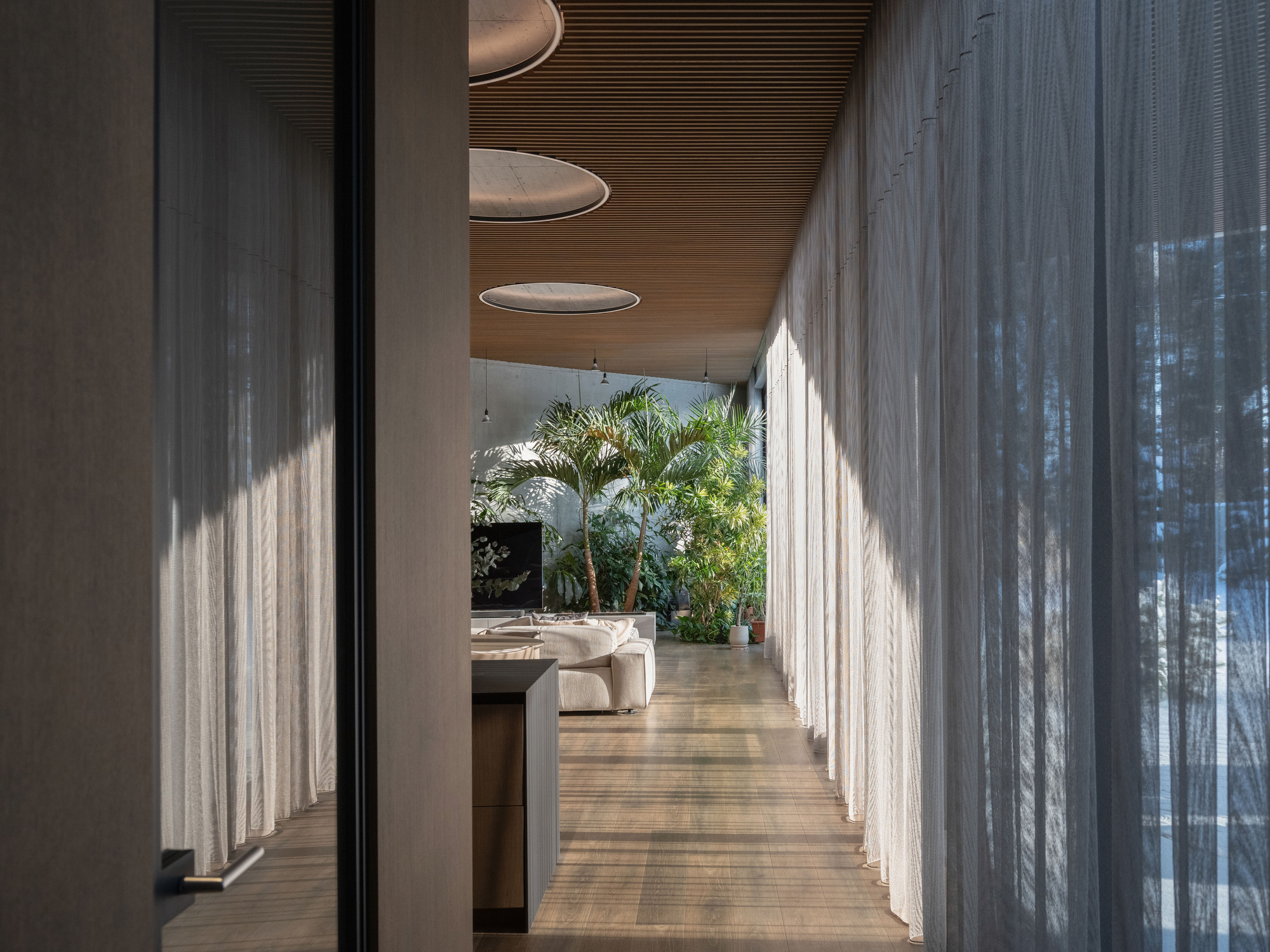 Interior corridor with slatted timber ceiling, sheer curtains, and dappled light filtering through