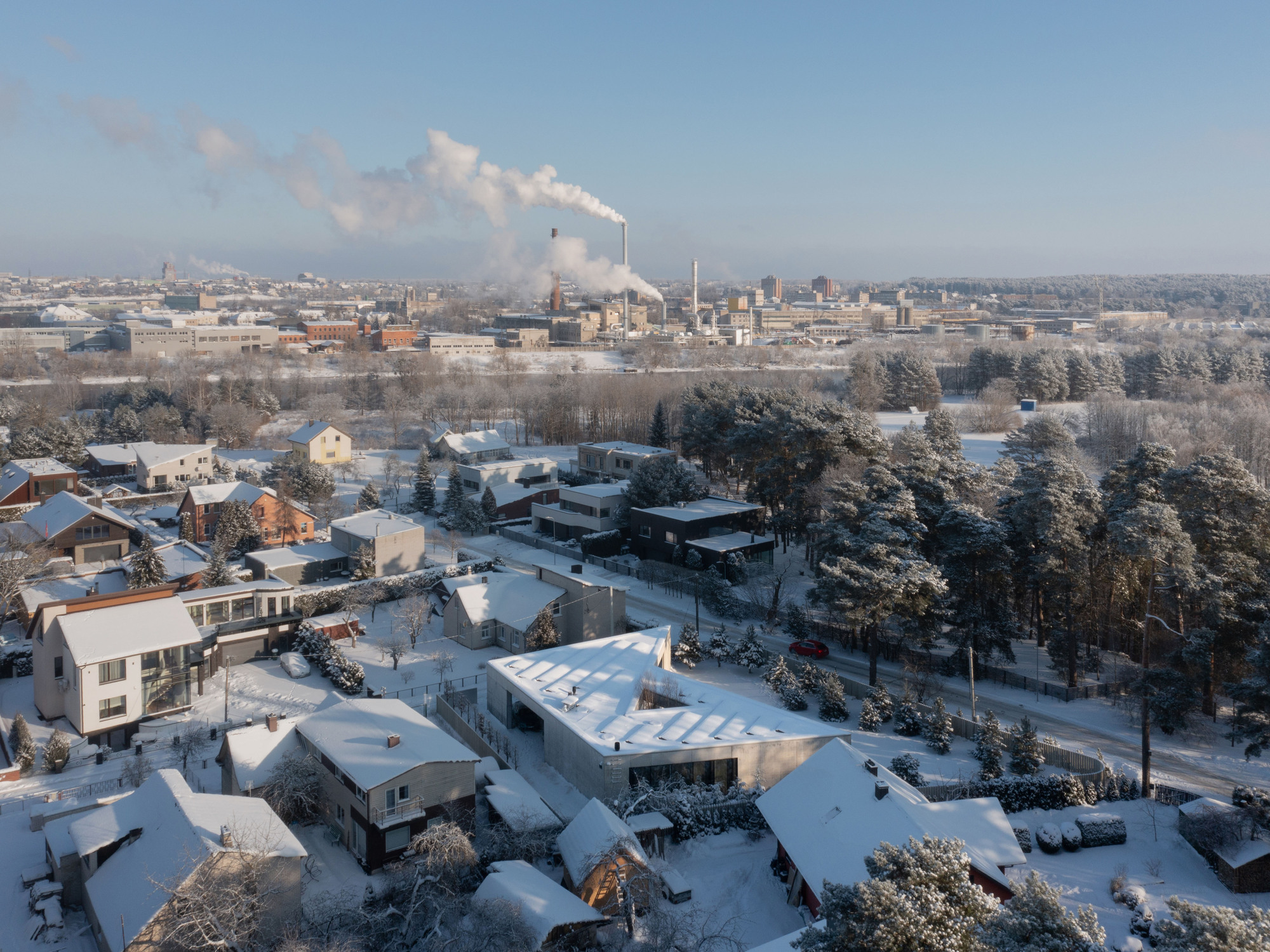 Drone view of the ribbed roof among snow-covered houses with industrial smokestacks on the distant horizon