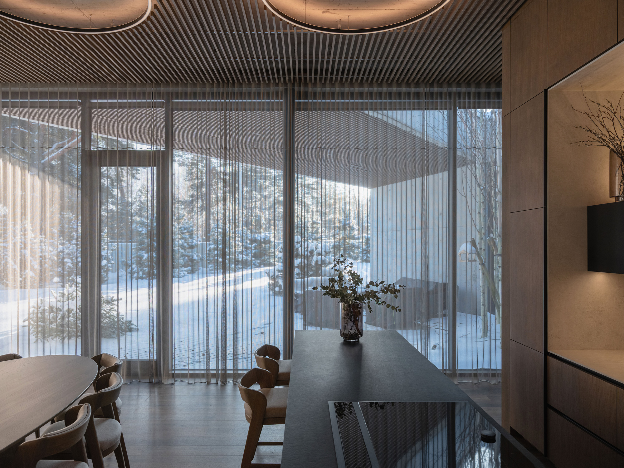 Dining area with timber slat ceiling and sheer curtains framing winter views beyond the glazing