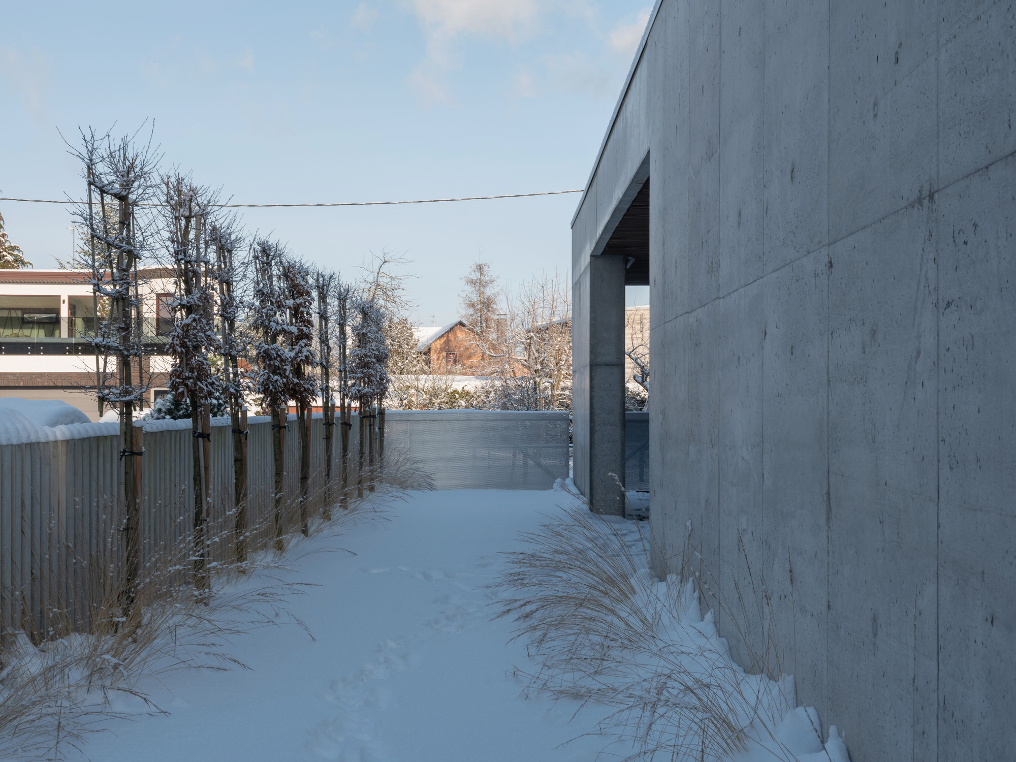 Concrete wall with recessed entrance alongside a snow-covered path and timber fence in winter
