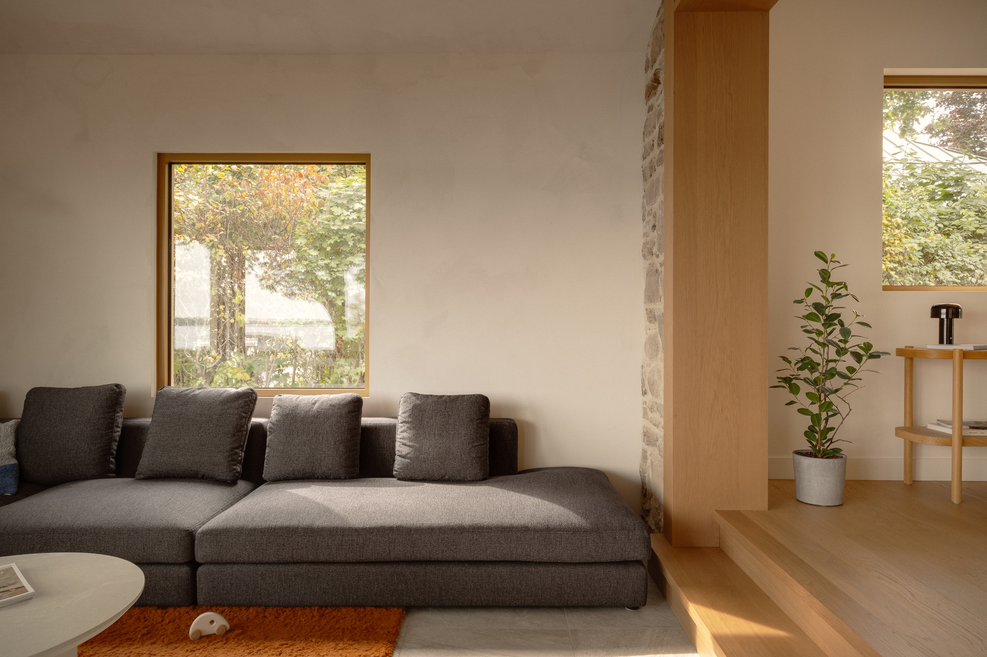 Living room with grey sectional sofa and timber-framed window overlooking trees in autumn light