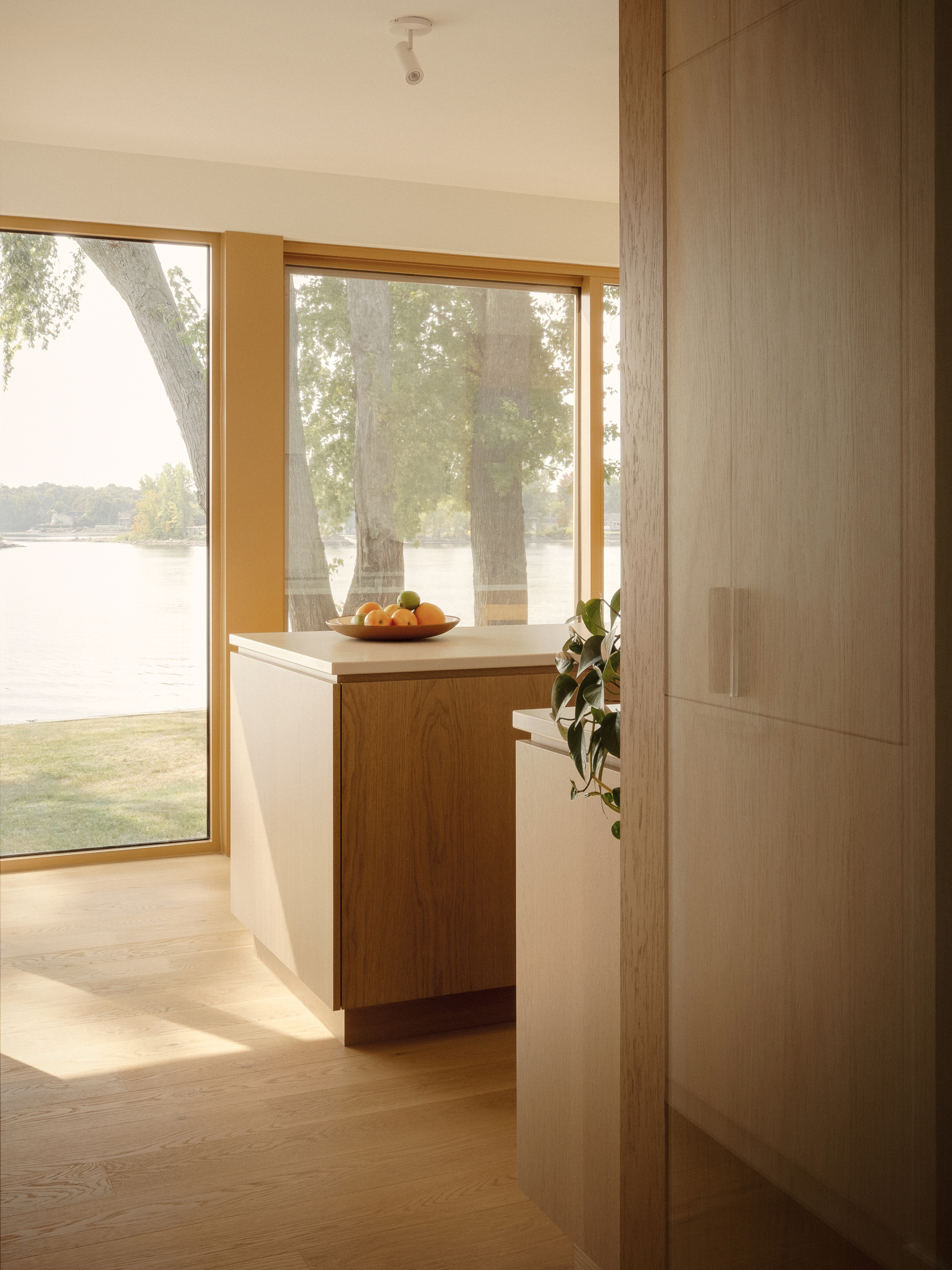 Hallway corner with oak storage cabinet and timber-framed window overlooking a lakeside lawn