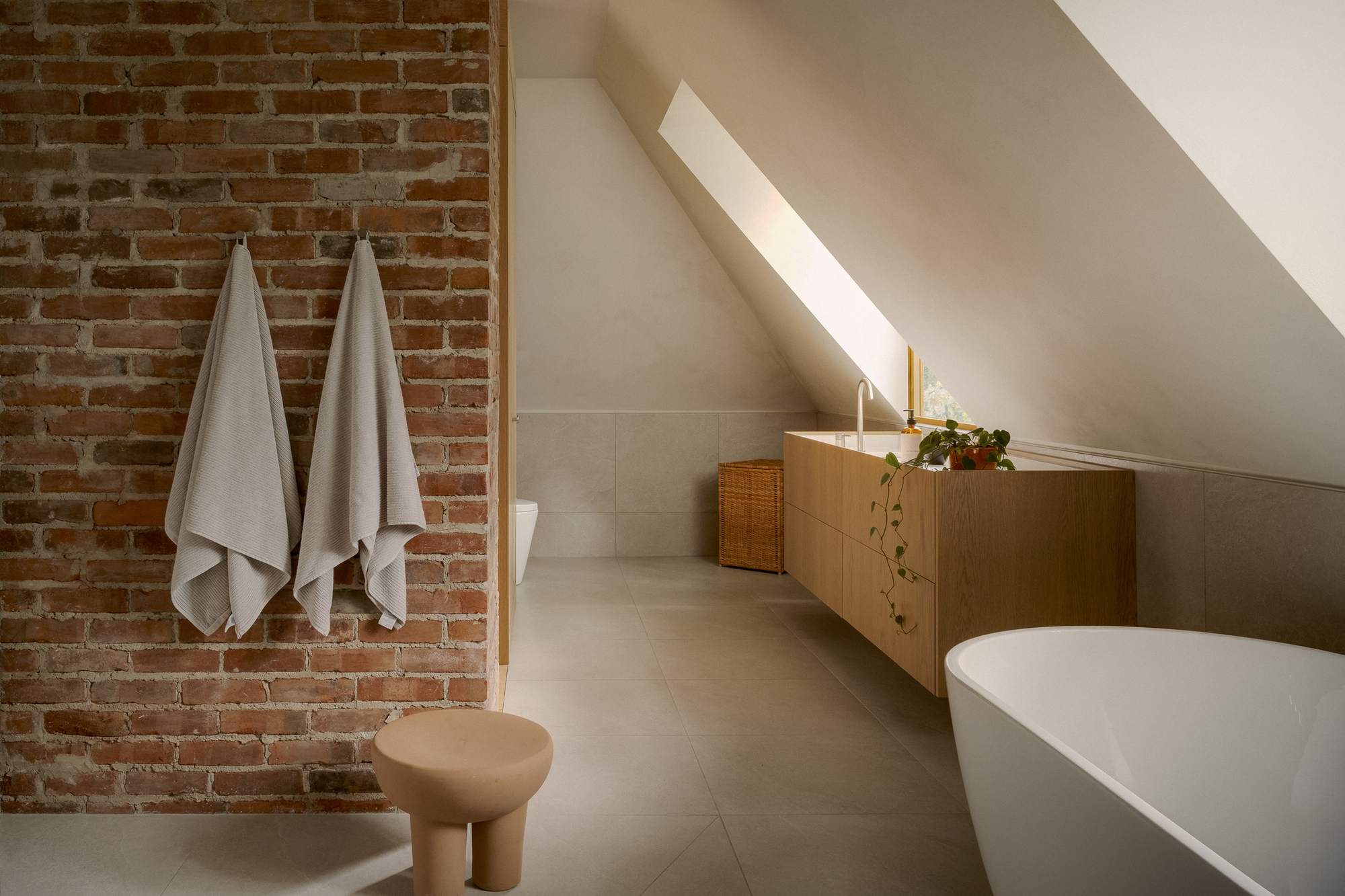 Attic bathroom with exposed brick wall and a skylight cutting across the ceiling plane