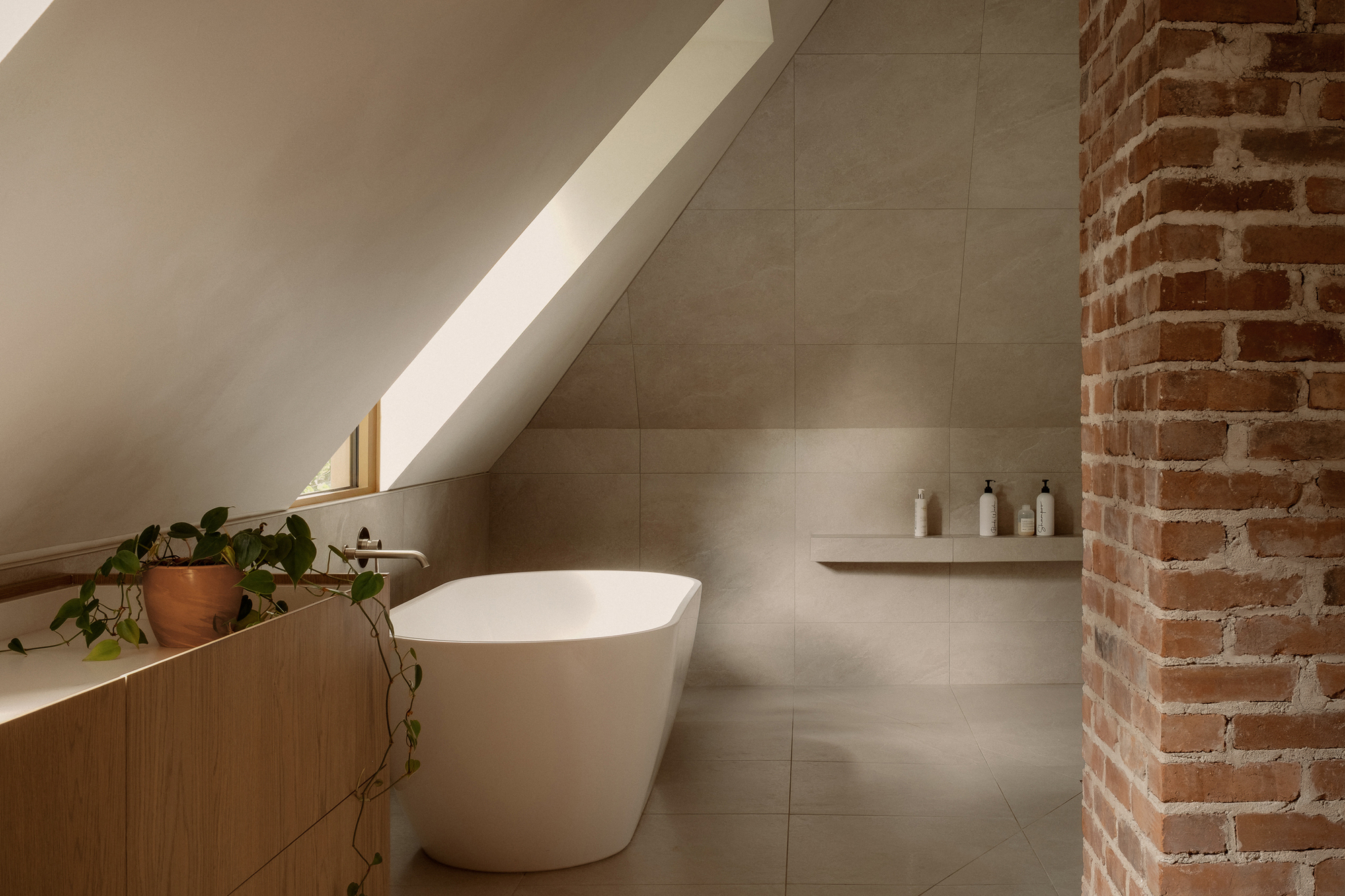 Freestanding bathtub beneath a linear skylight alongside an exposed brick column