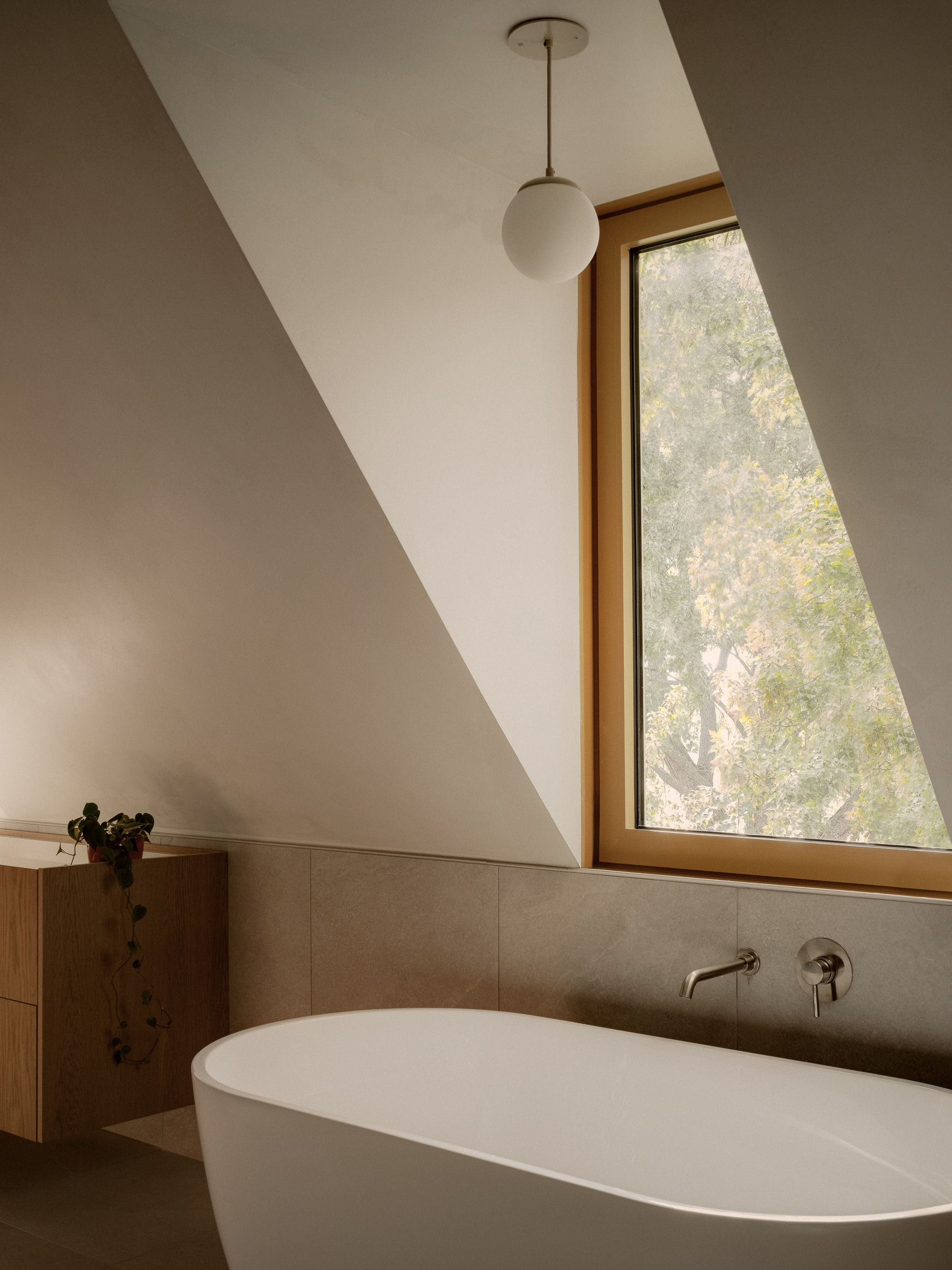 Triangular window framing autumn foliage above a tub with wall-mounted faucet