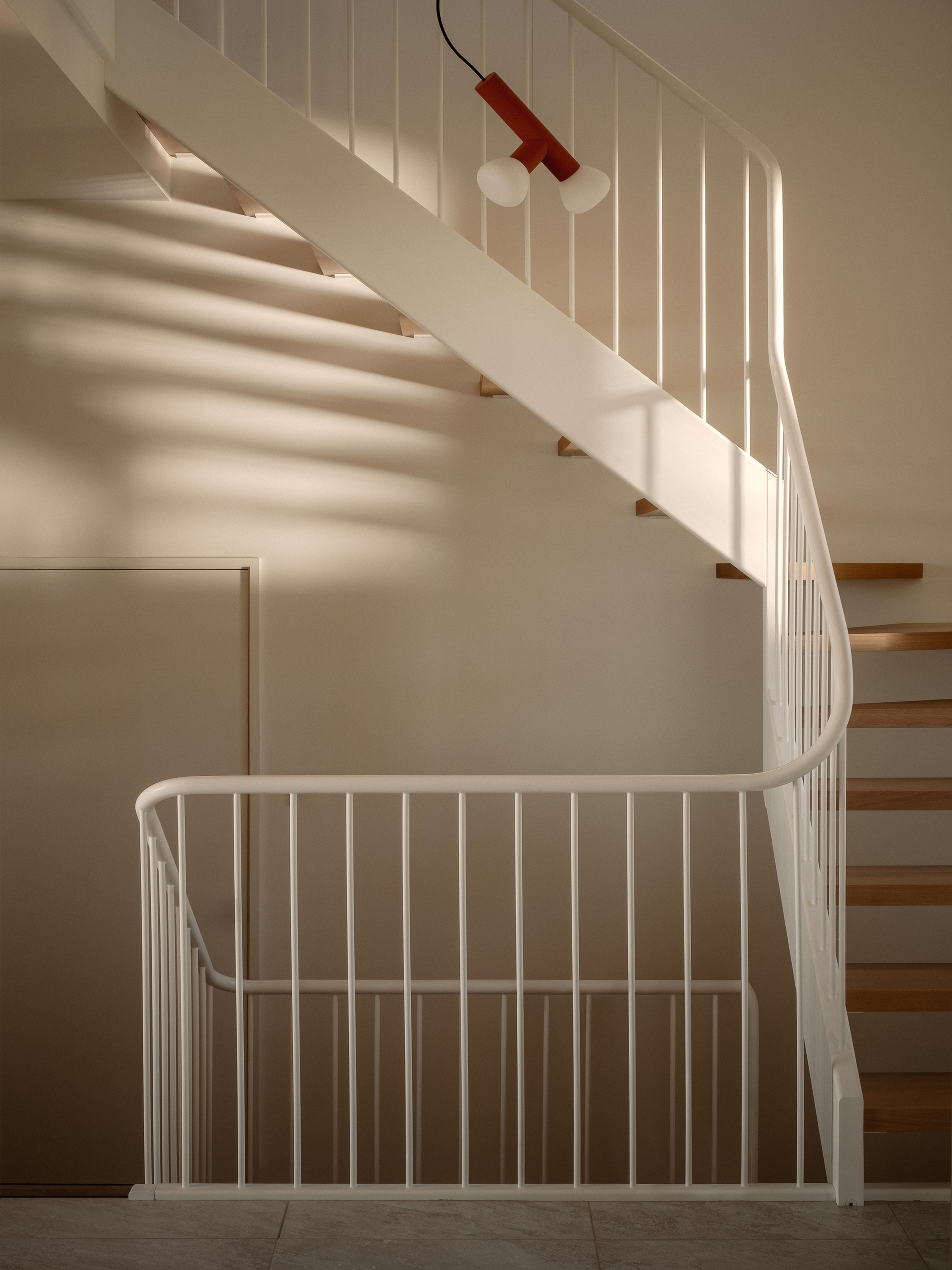 Curved staircase with white metal balustrade and timber treads beneath a red pendant light