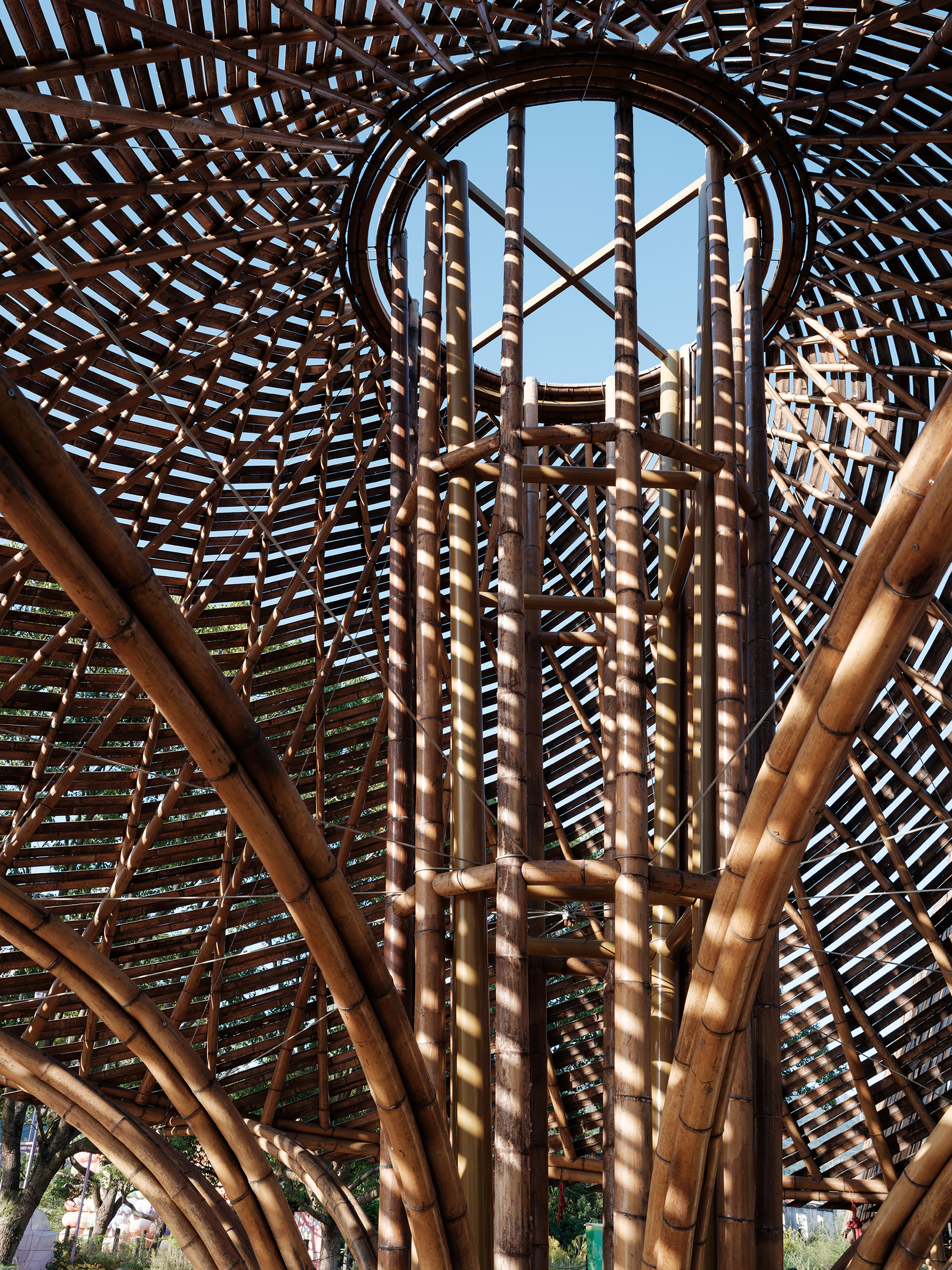 Interior view looking up through bundled bamboo columns and latticed roof structure to a circular oculus