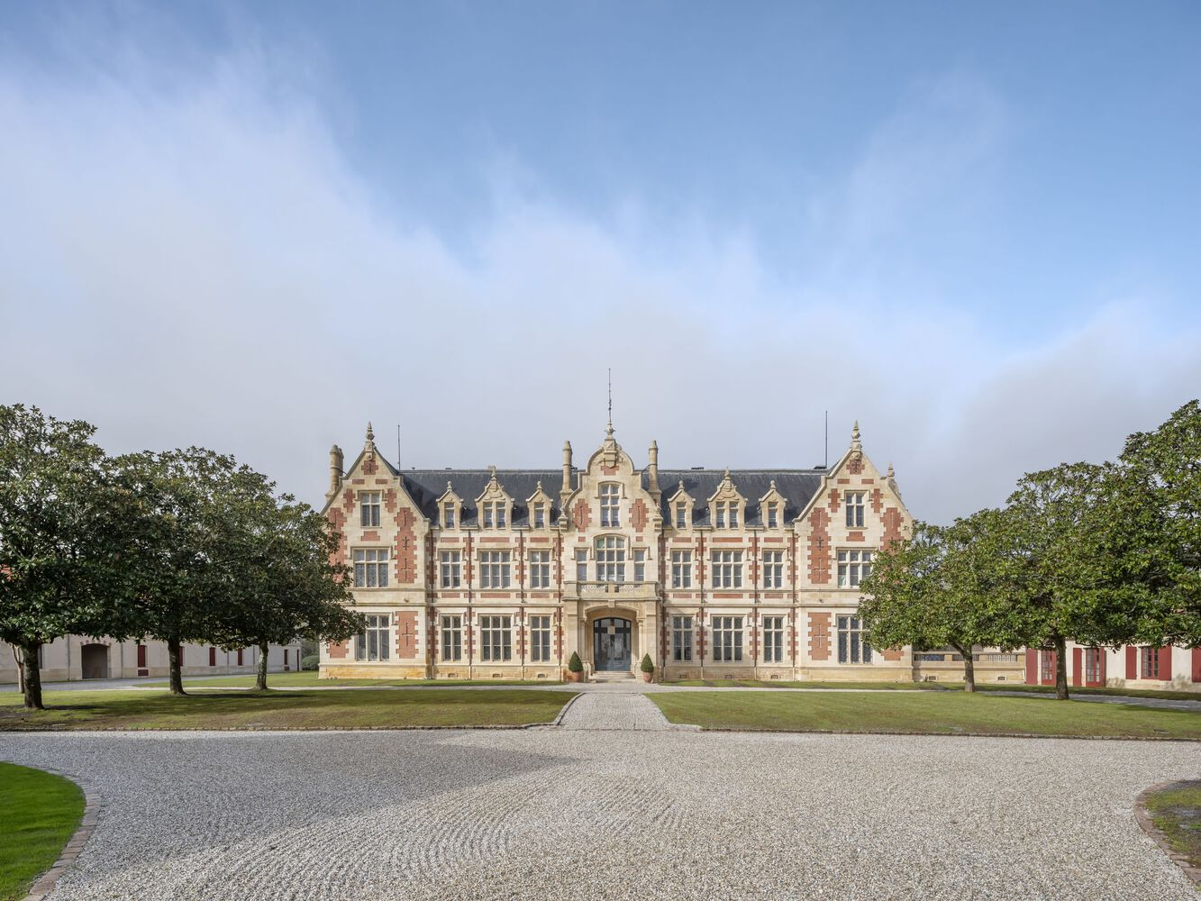 Symmetrical facade of red brick and pale stone building with central gable and gravel forecourt