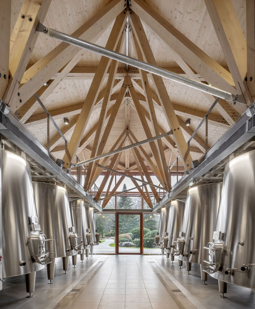 Central aisle flanked by stainless steel fermentation vessels beneath exposed timber roof trusses
