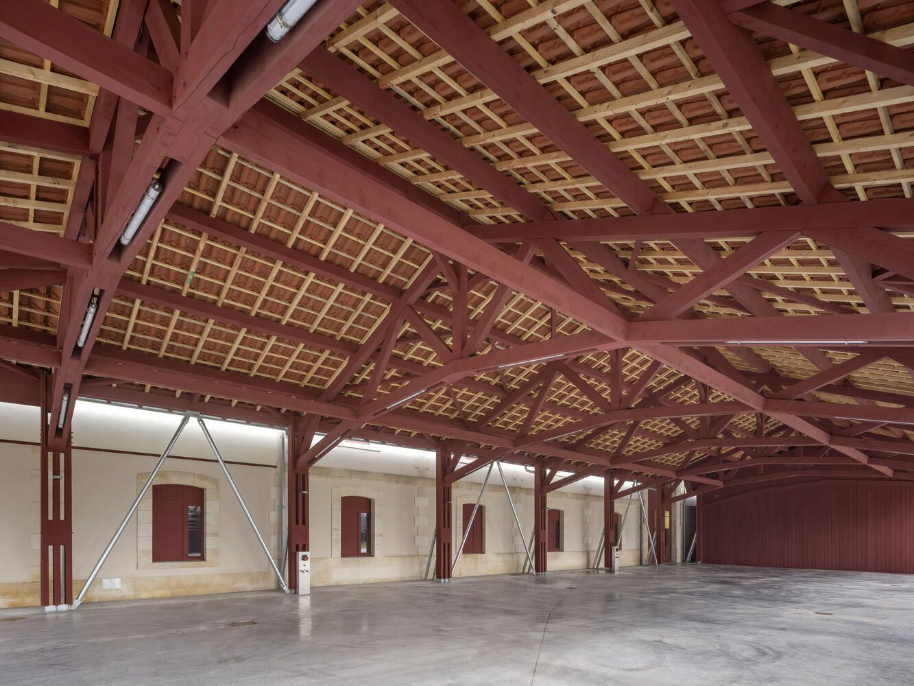 Interior showing red-painted timber truss system with gridded ceiling infill and cable bracing