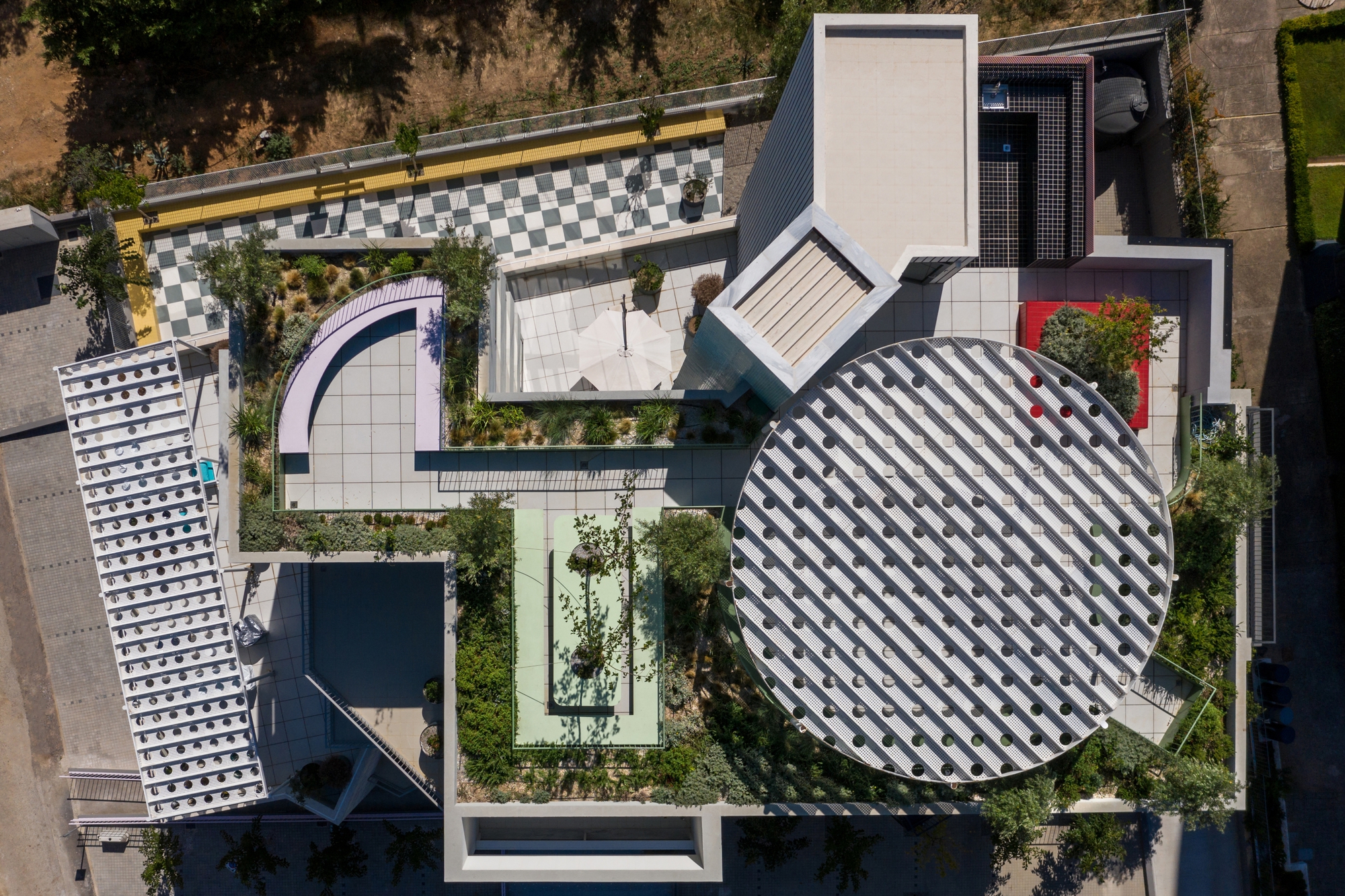 Aerial view showing the circular checkered roof alongside rectangular volumes and courtyard gardens with planted trees