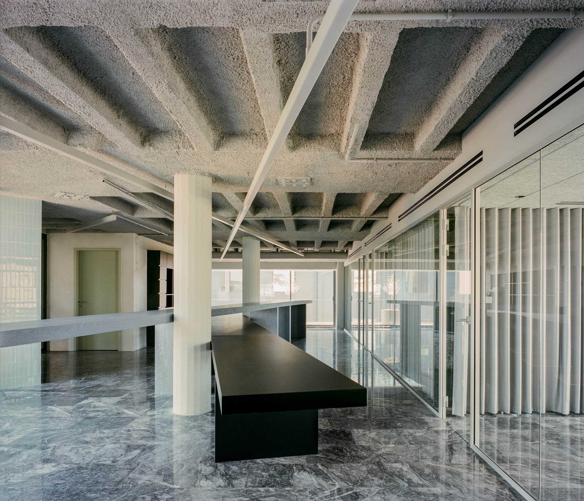 Interior workspace with exposed coffered concrete ceiling, white columns, black tables and marble flooring