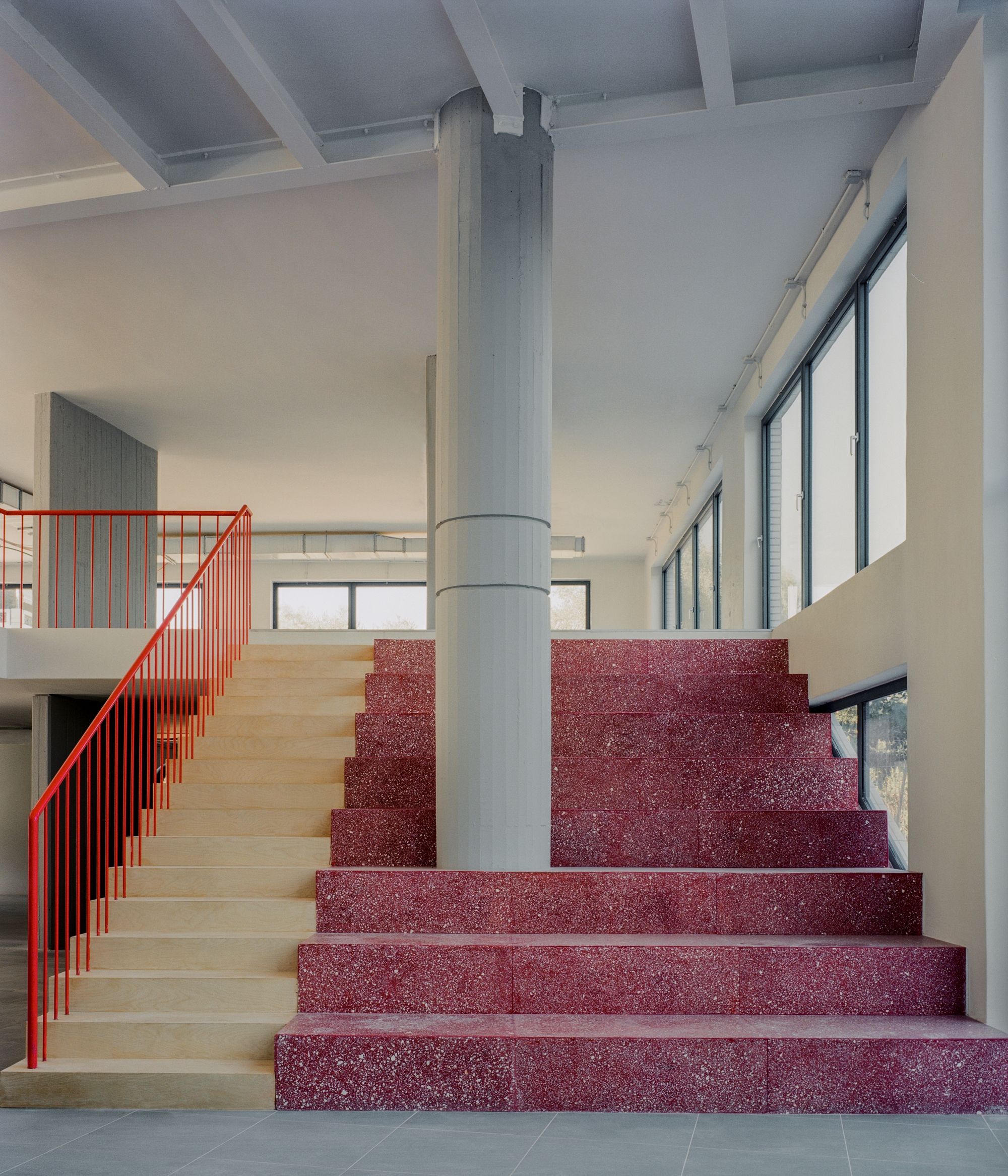 Lobby staircase with red terrazzo treads, light wood risers, red metal railing and central cylindrical column